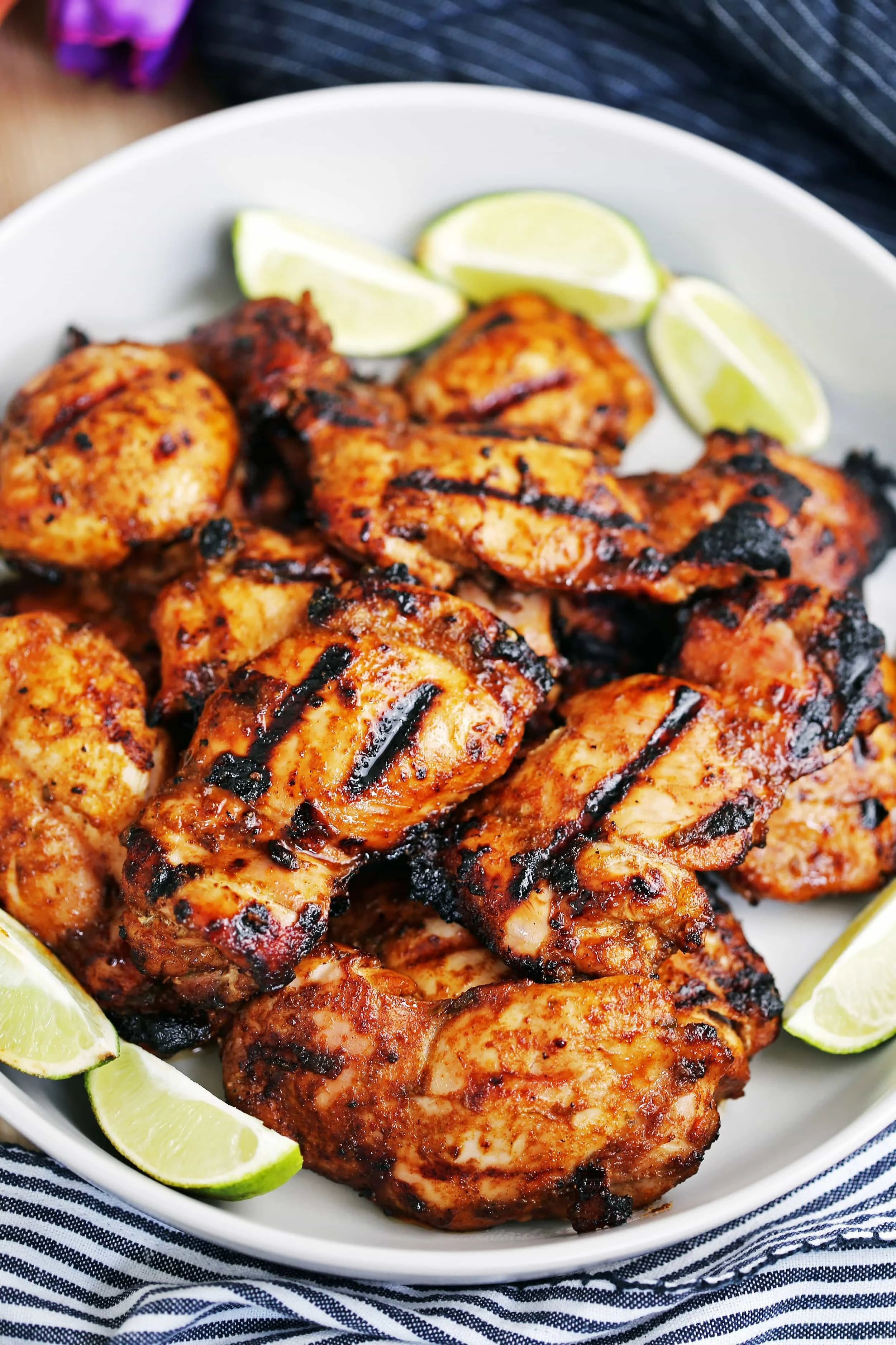 A dozen hot grilled chili lime chicken thighs surrounded by lime wedges on a large grey platter.