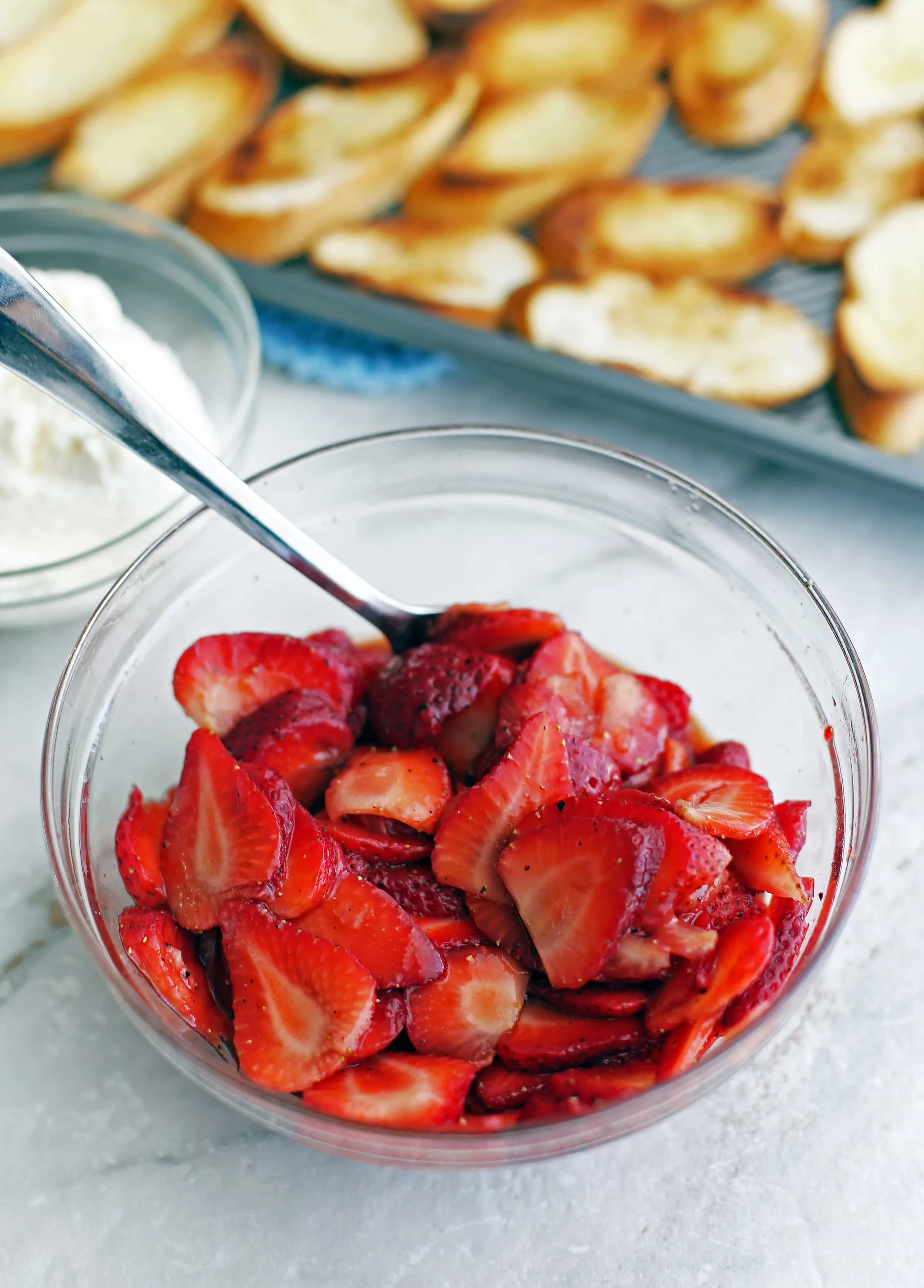 A glass bowl of sliced strawberries that's combined with balsamic vinegar, sugar, and black pepper.