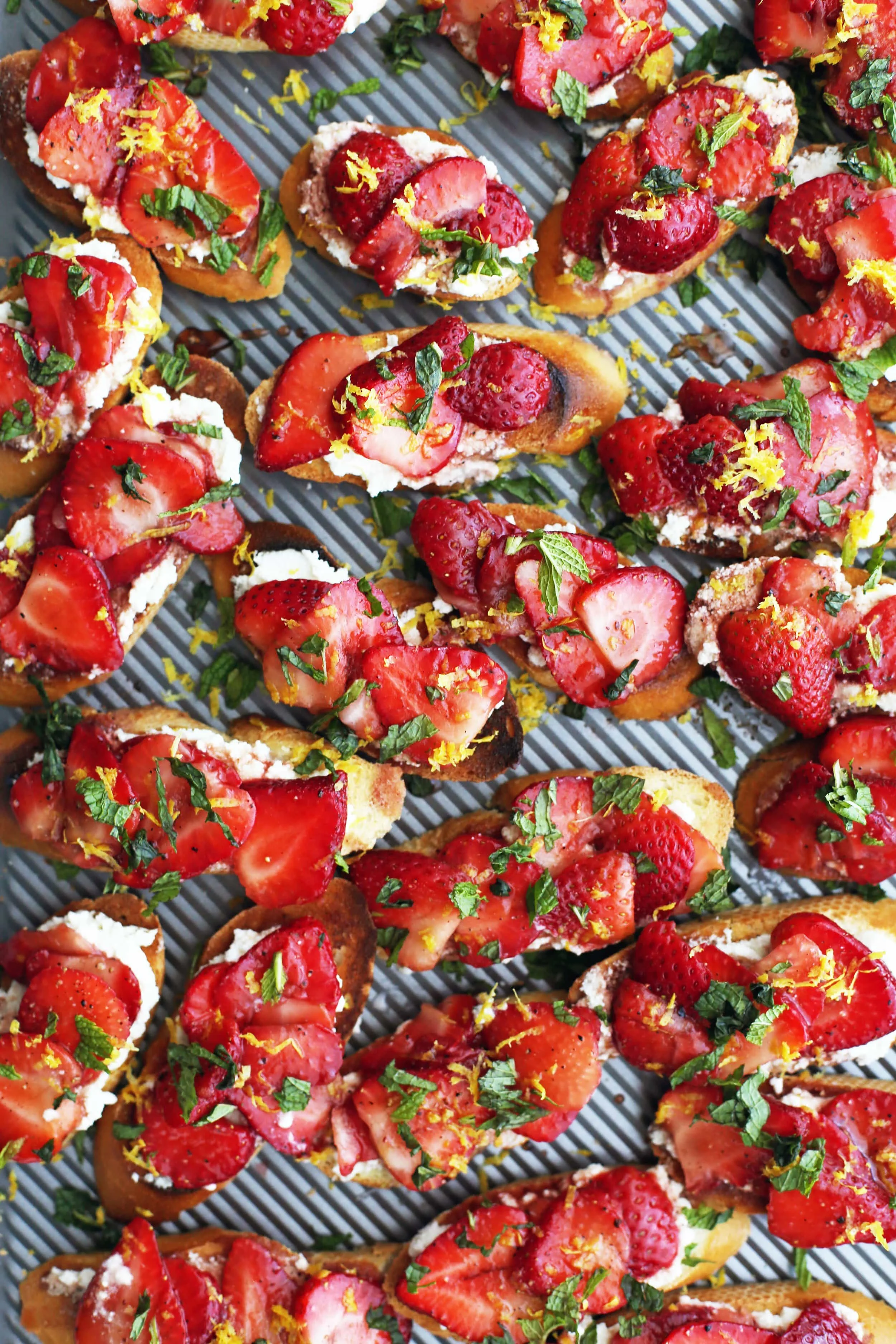 A baking sheet full of Balsamic Strawberry Ricotta Crostini with fresh lemon zest and mint on top.