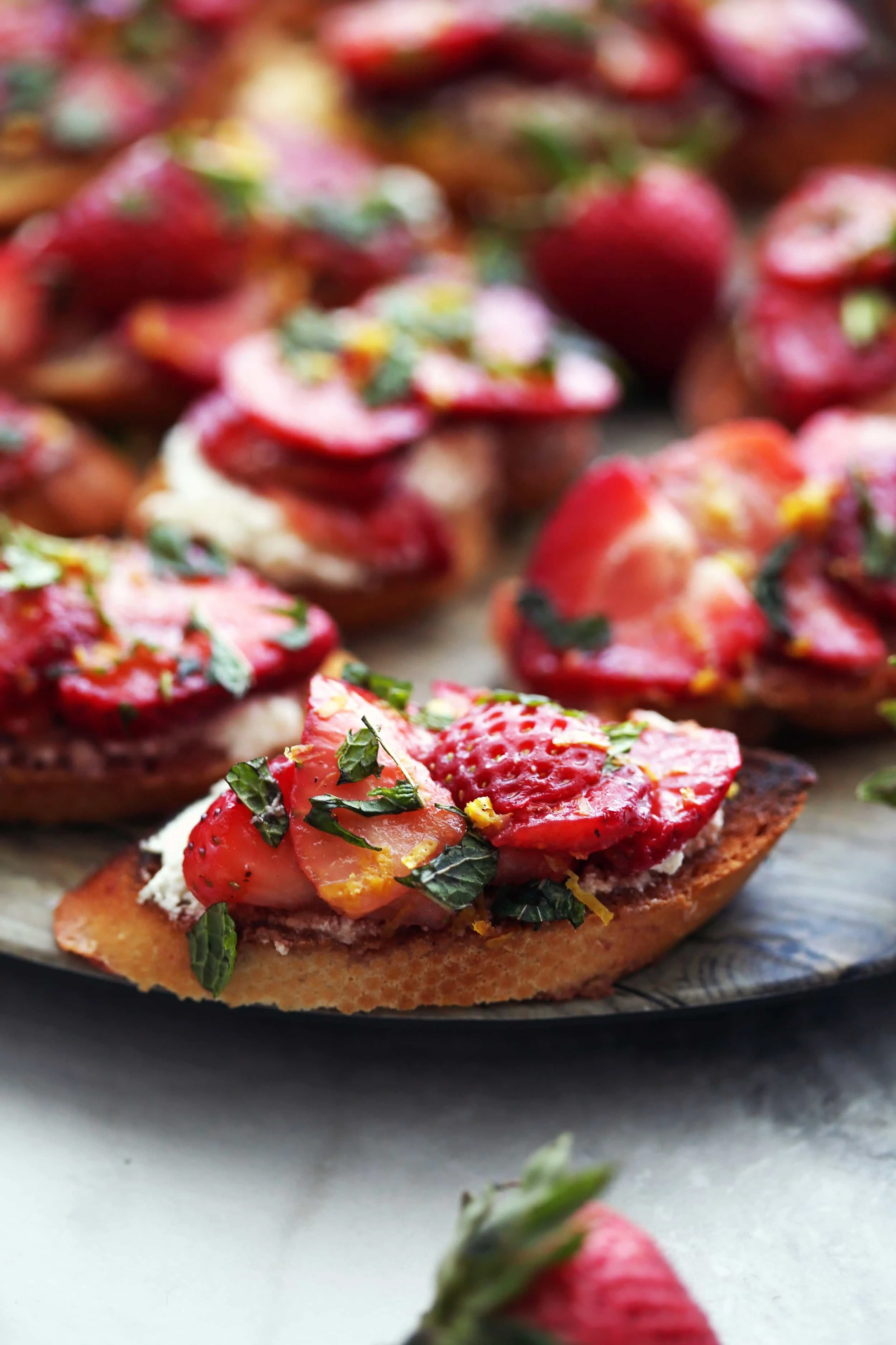 A closeup of a single Balsamic Strawberry Ricotta Crostino with more crostini behind it that's on a large round platter.