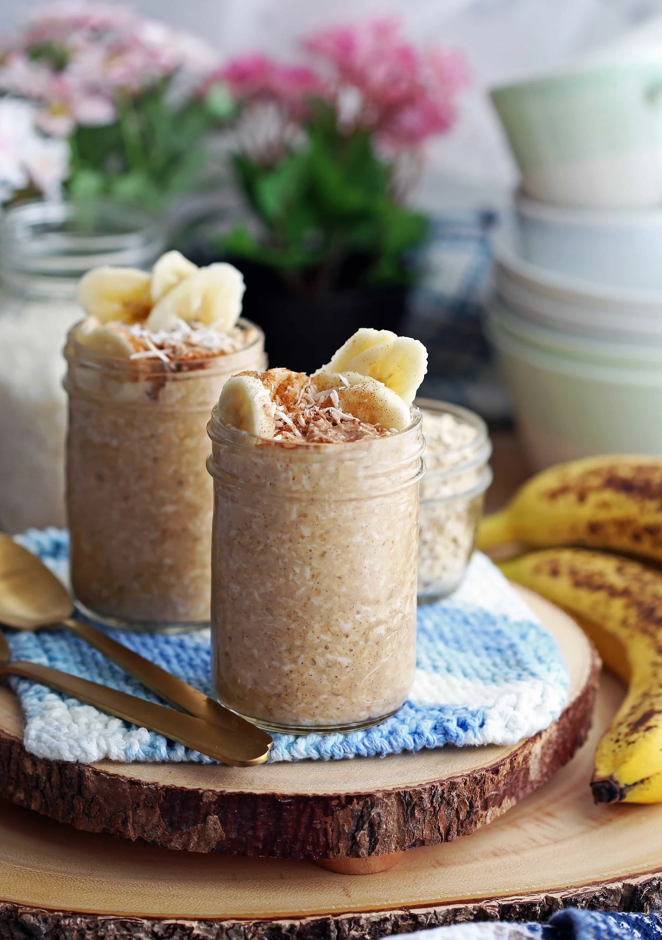 Banana Coconut Cream Pie Overnight Oats in two mason jars on a wooden platter.