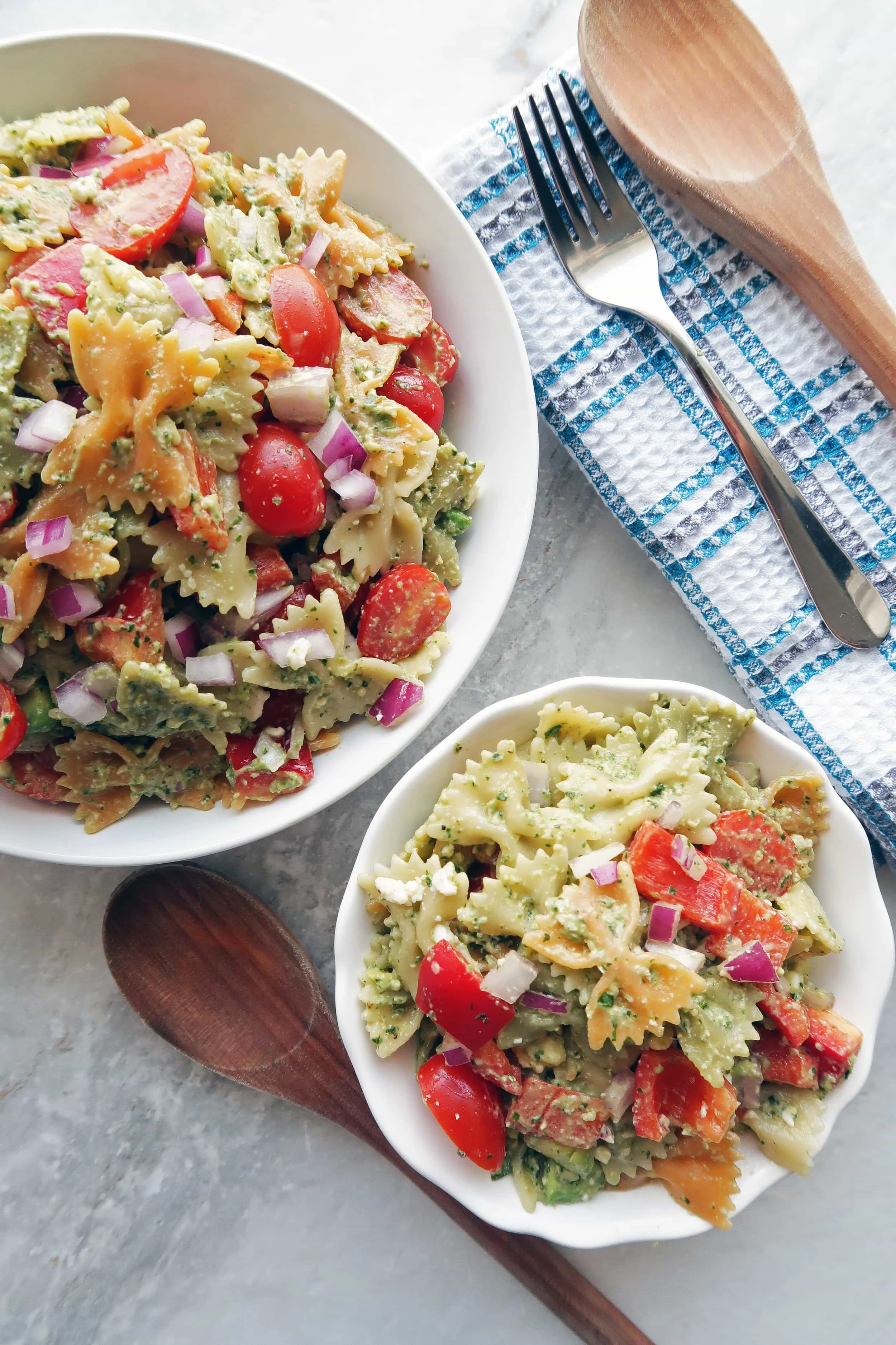 Overhead view of basil avocado pesto vegetable pasta salad in a large bowl and a small bowl.