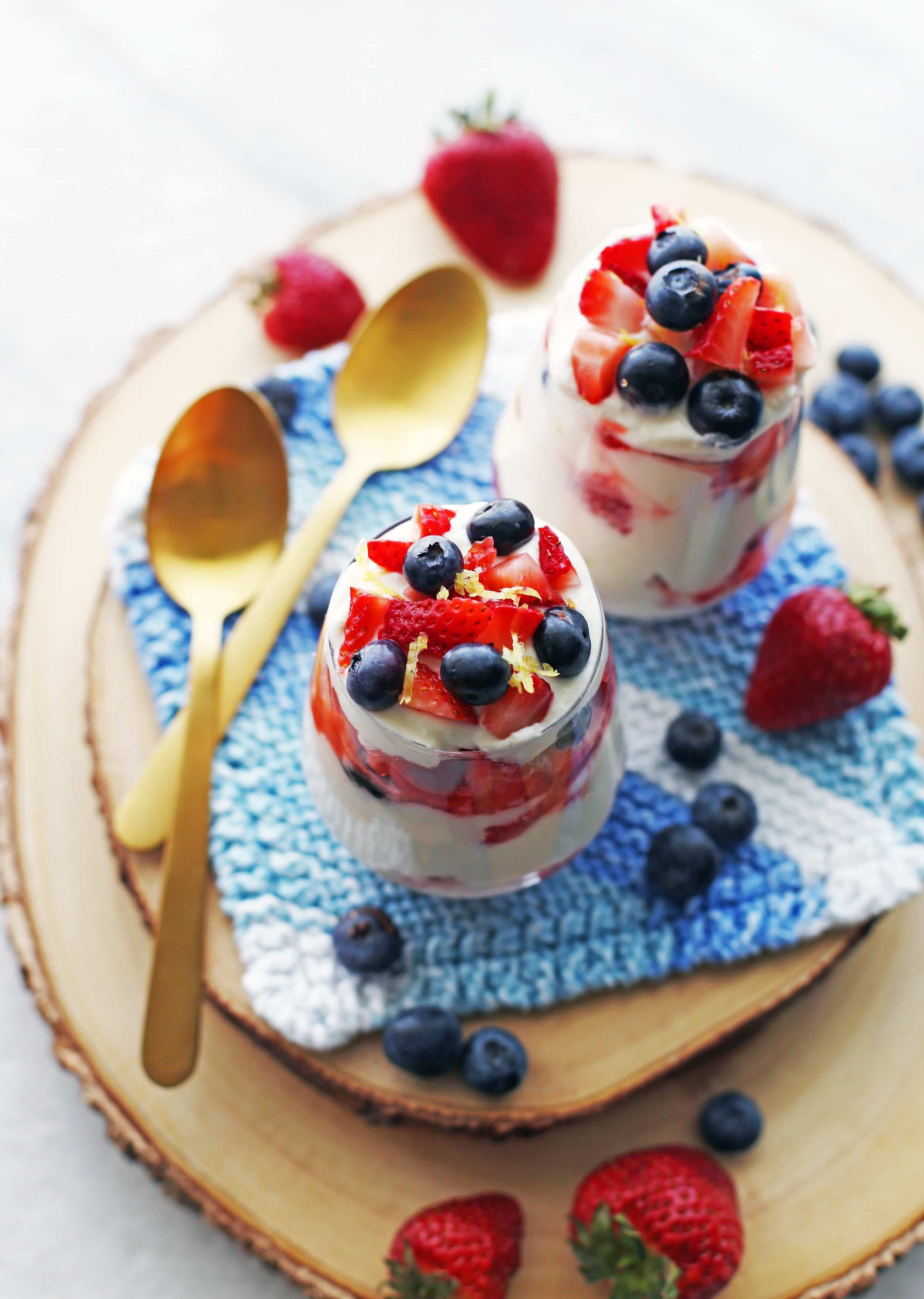 Two glasses full of layers of fresh strawberries, blueberries, and honey lemon mascarpone cream.