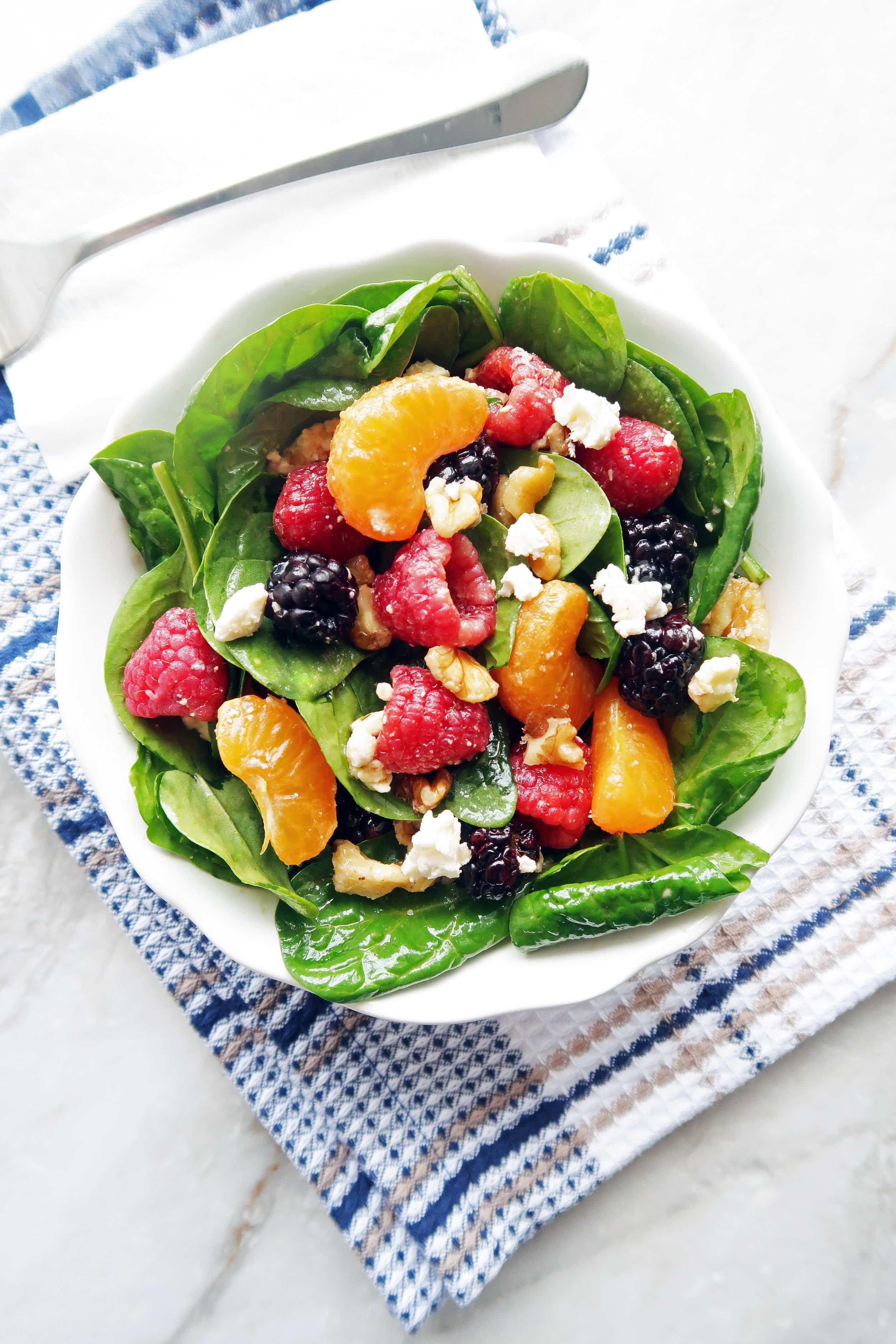 Berry Orange Spinach Salad with Citrus Balsamic Vinaigrette in a small white bowl that's on top of a kitchen towel.