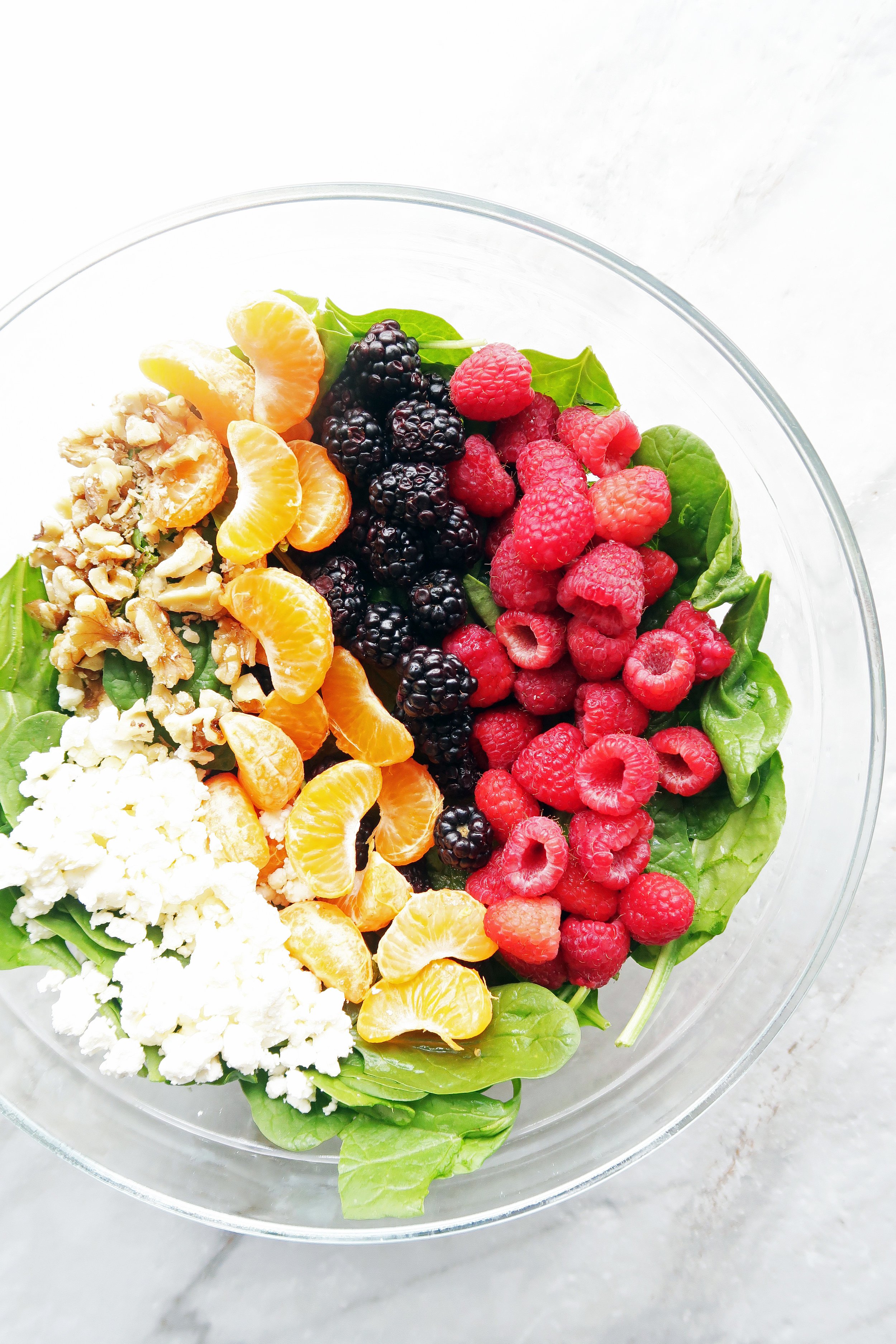 A bowl of spinach, blackberries, raspberries, mandarin oranges, walnuts, and feta.