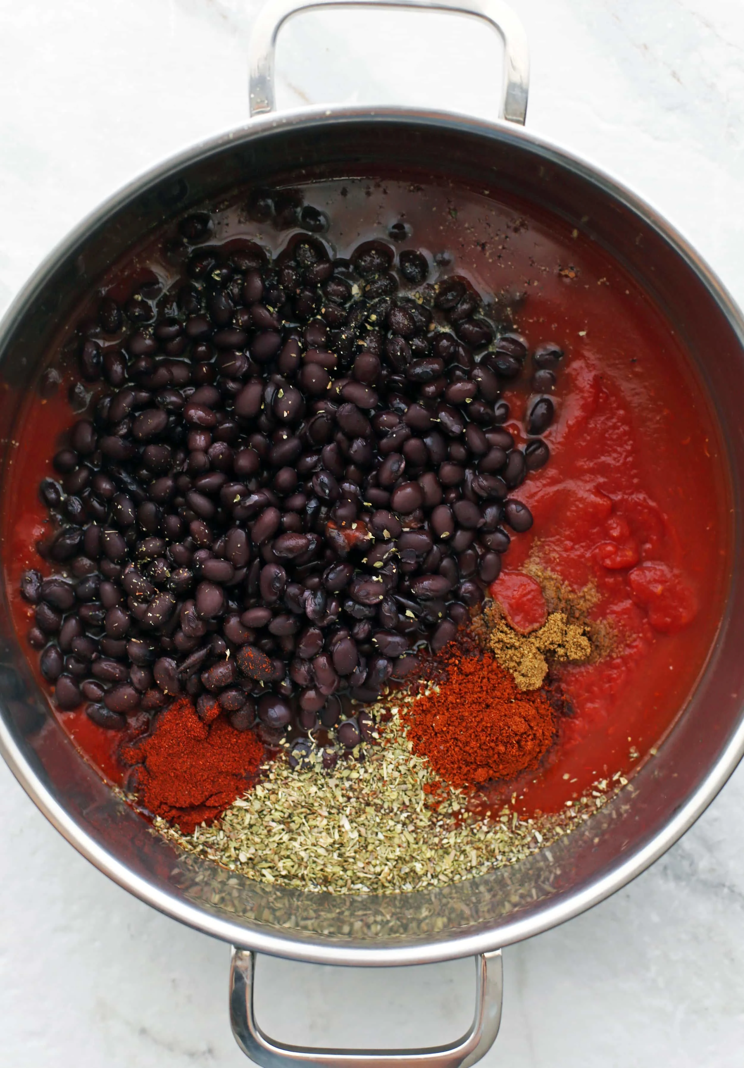 Black beans, spices, vegetable broth, and crushed tomatoes in a large metal pot.