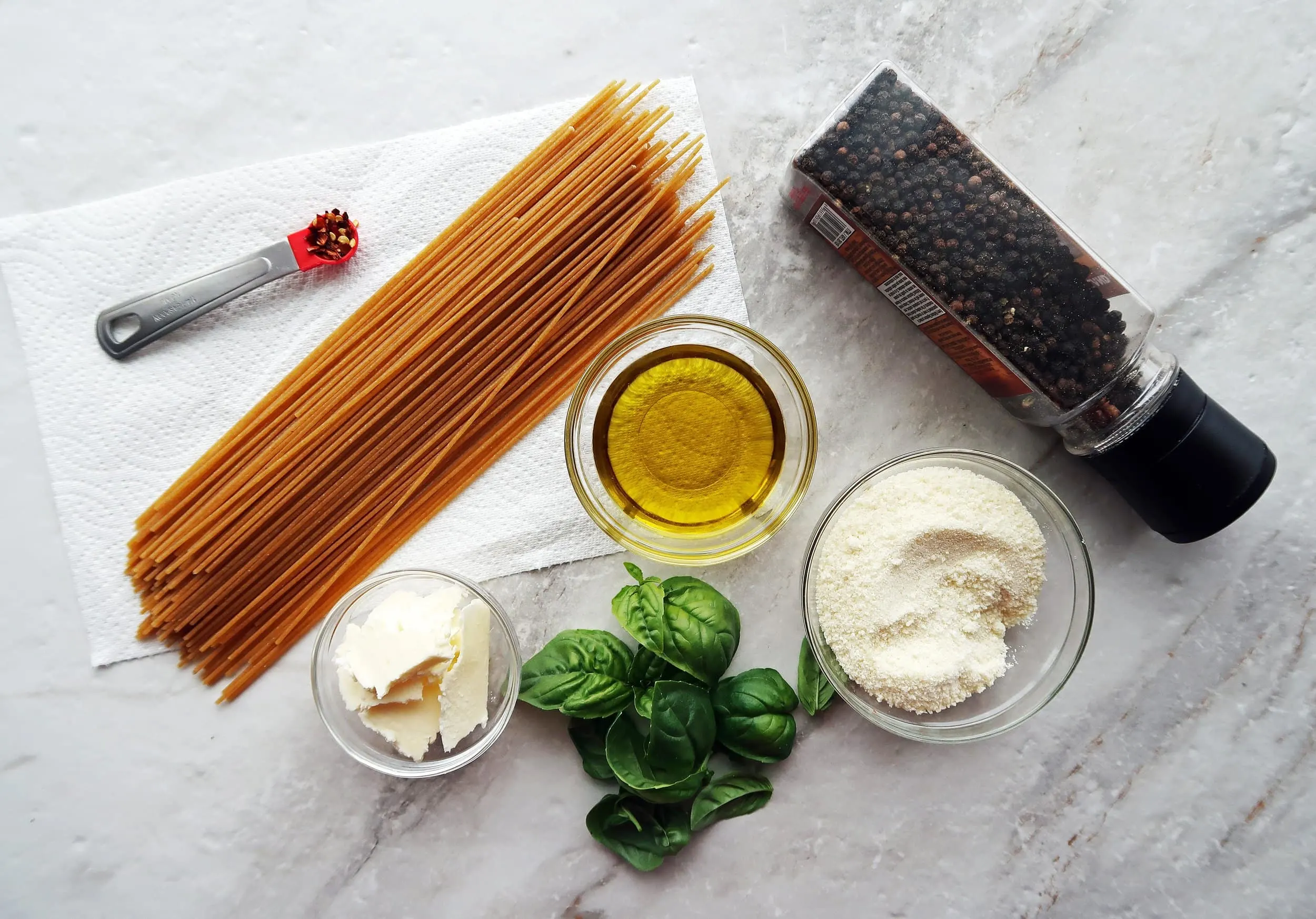 Whole wheat spaghetti next to basil, parmesan, olive oil, butter, and black pepper.