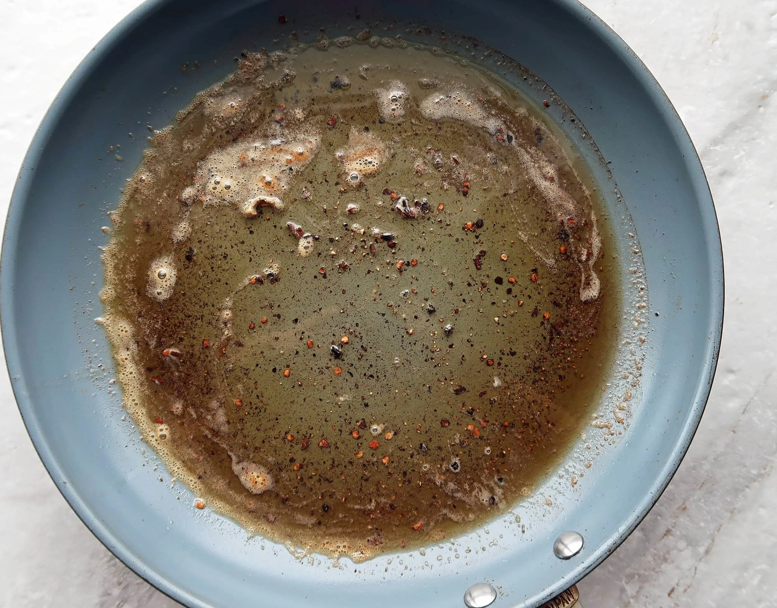 A skillet with melted butter, olive oil, black pepper, and red pepper flakes.