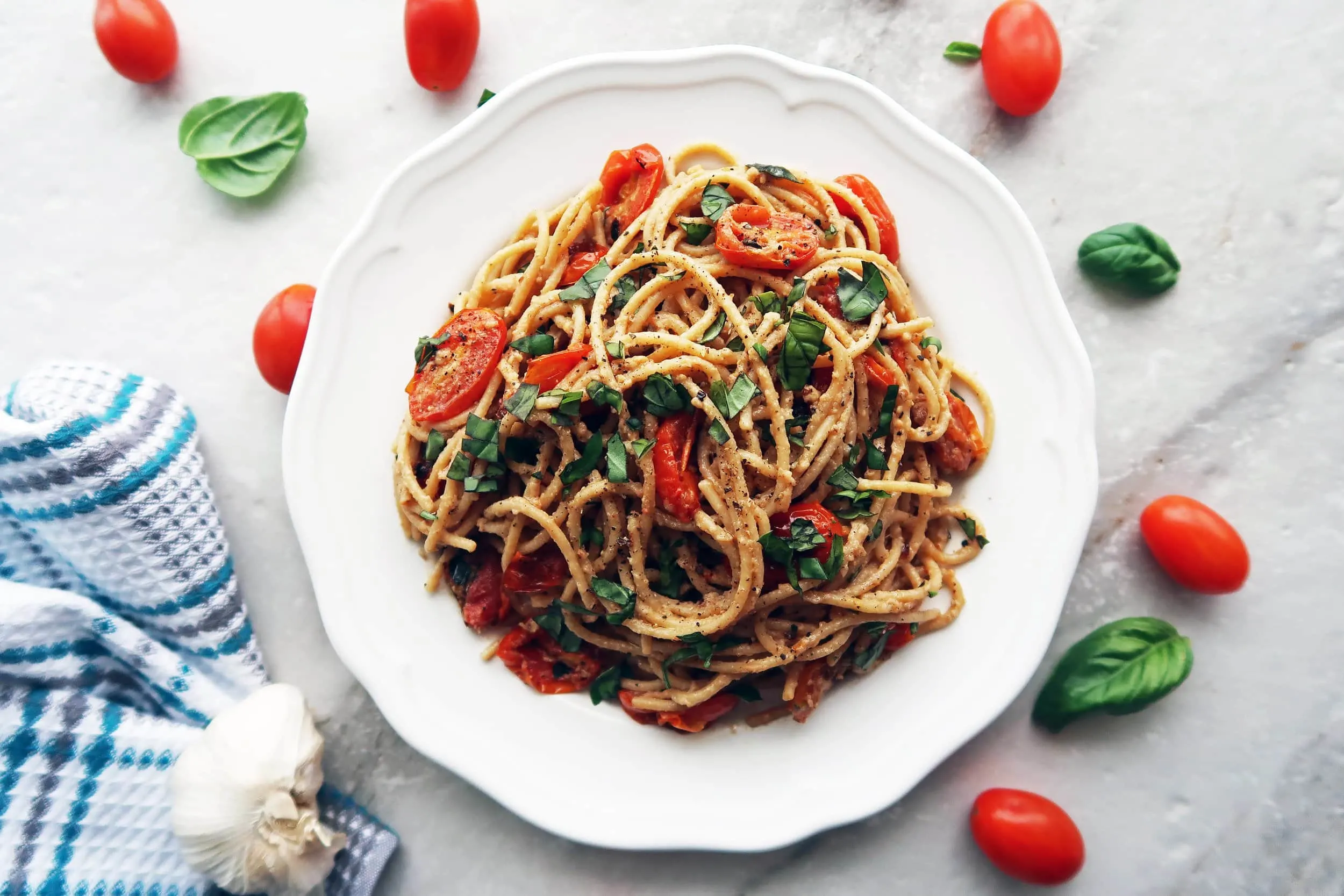 Black Pepper and Parmesan Spaghetti with Garlic Roasted Tomatoes and basil aka cheese and pepper pasta on a white plate.