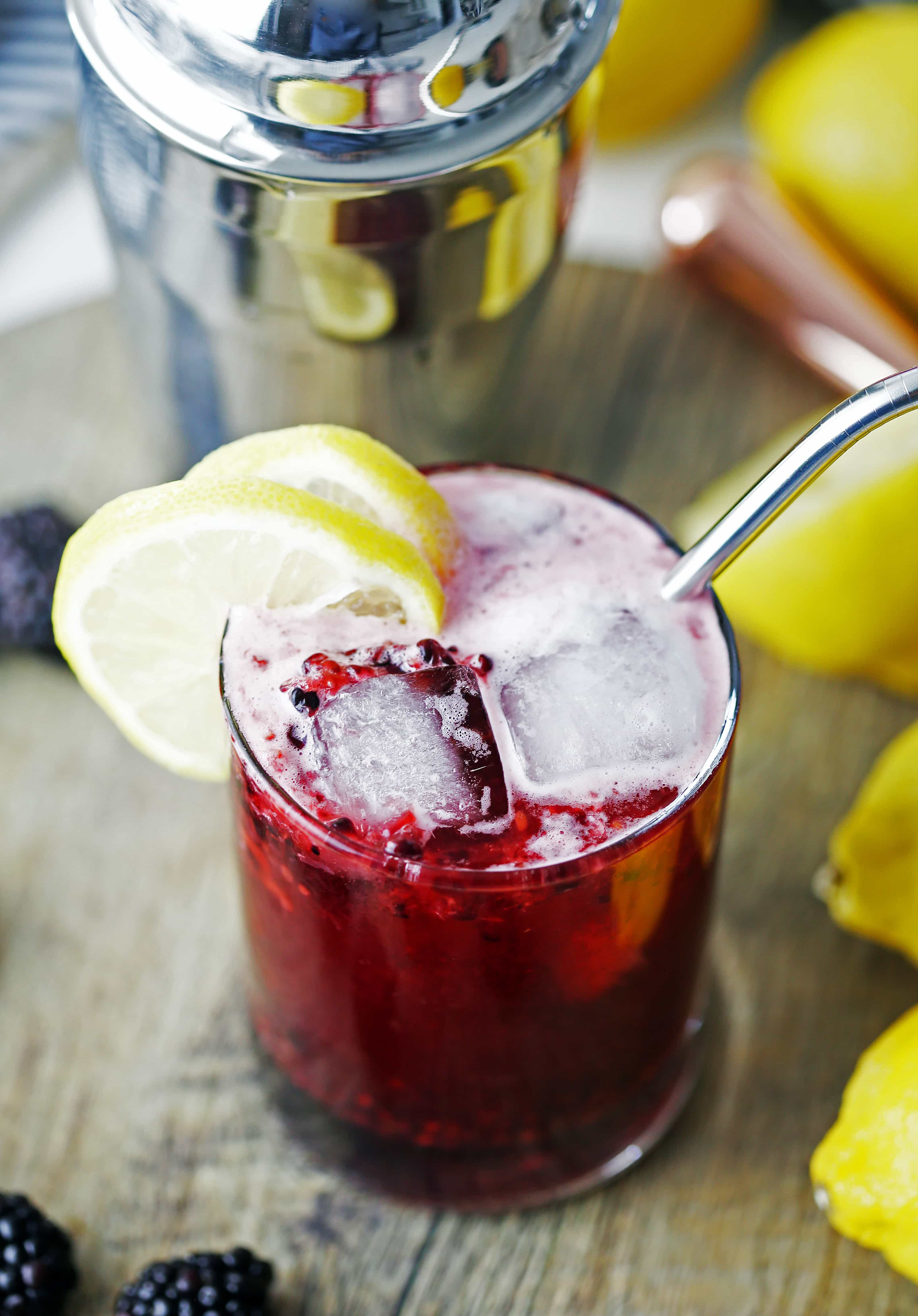 An overhead view of a glass of blackberry lemon smash cocktail with lemon slices and a straw in it.