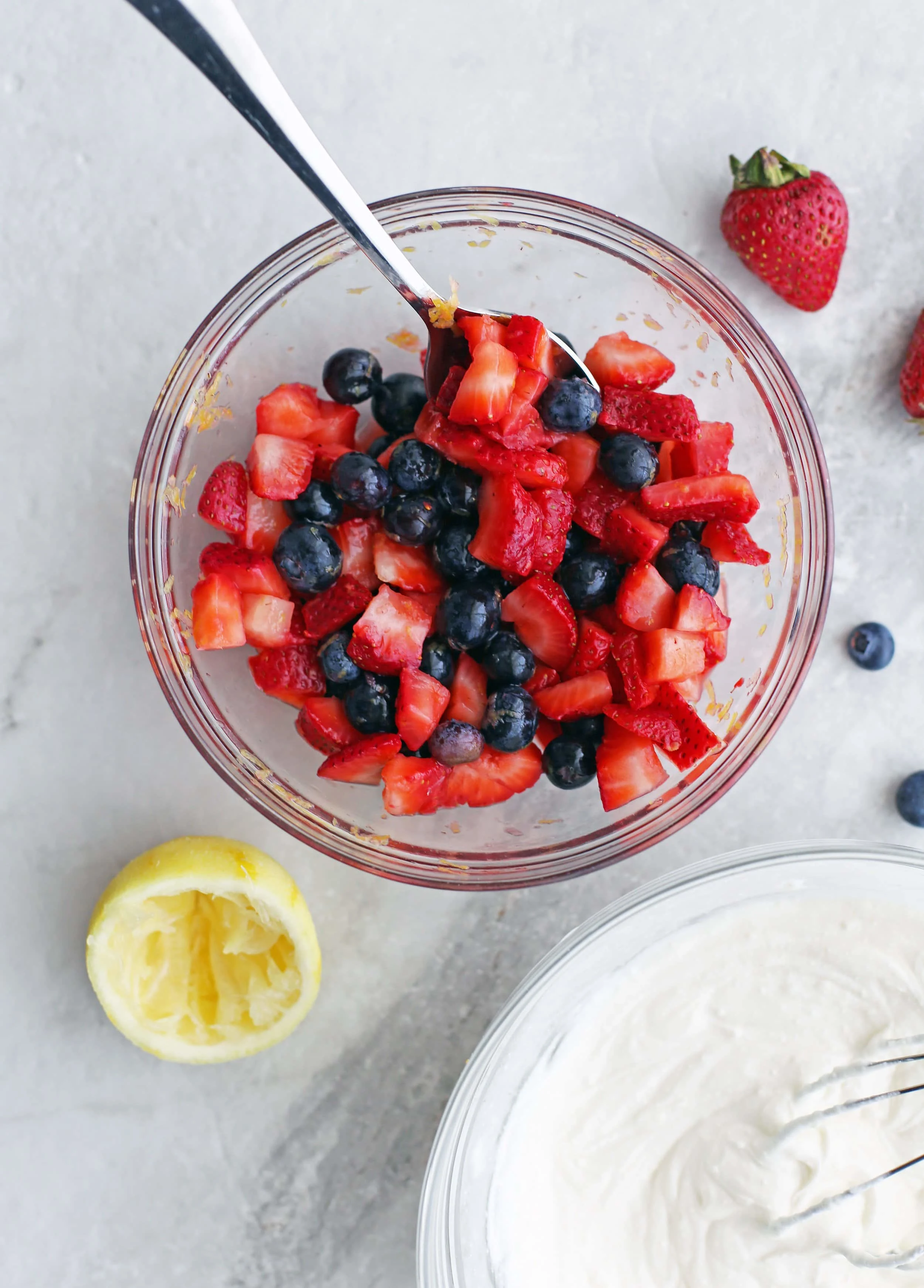 Sliced strawberries, blueberries,lemon juice and lemon zest in a glass bowl.