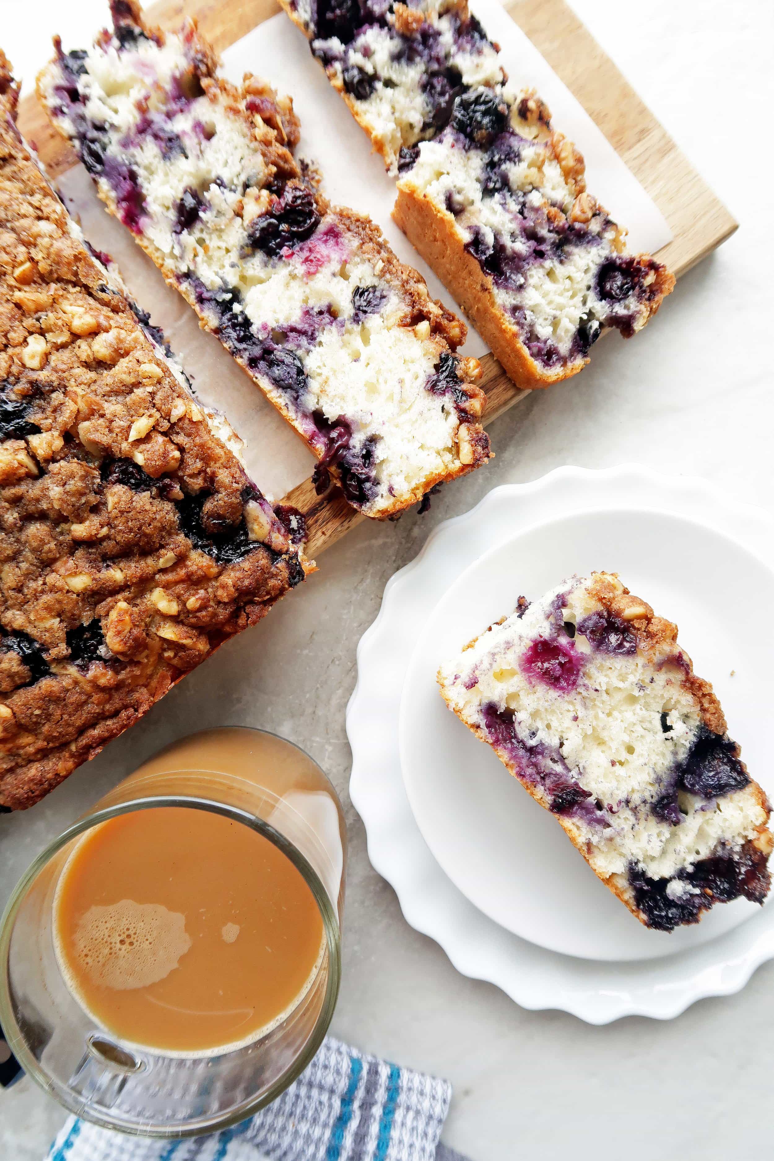 Blueberry coffee cake with crumble on a wooden board and a slice on a white plate.