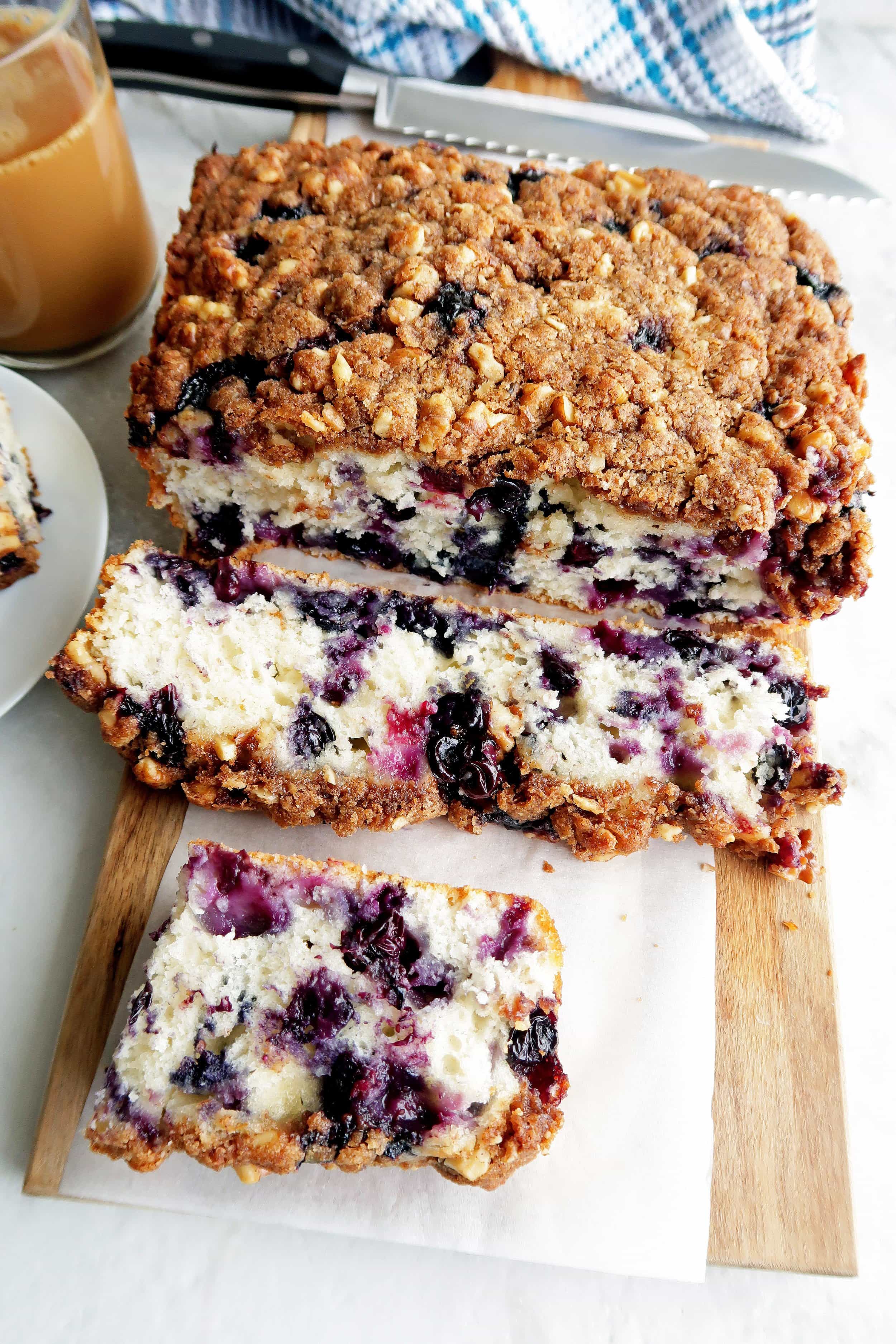 Sliced blueberry coffee cake with brown sugar-walnut crumble on a long wooden board.