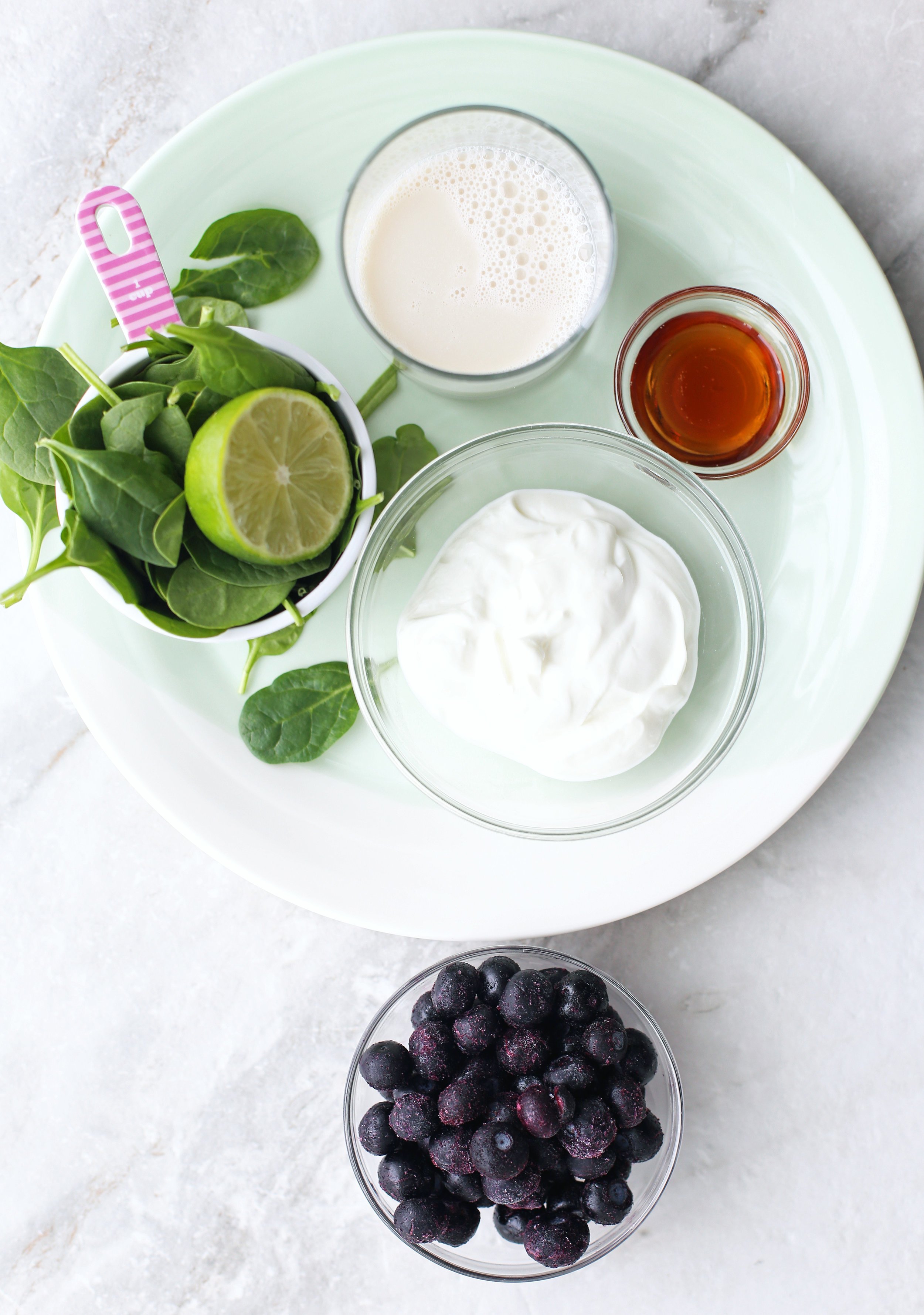 Bowls of frozen blueberries, Greek yogurt, baby spinach, almond milk, maple syrup, and half a lime.