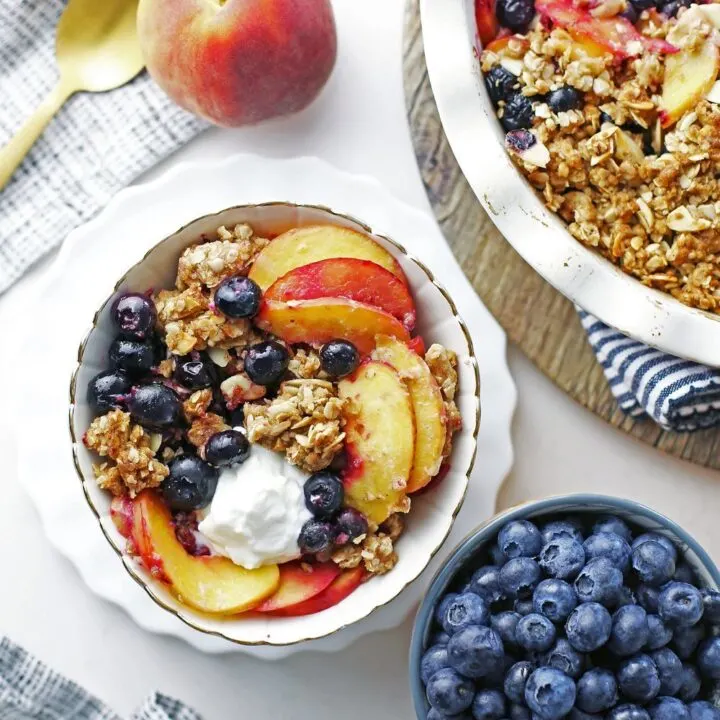Overhead view of a bowl of blueberry peach crisp with more on the side.