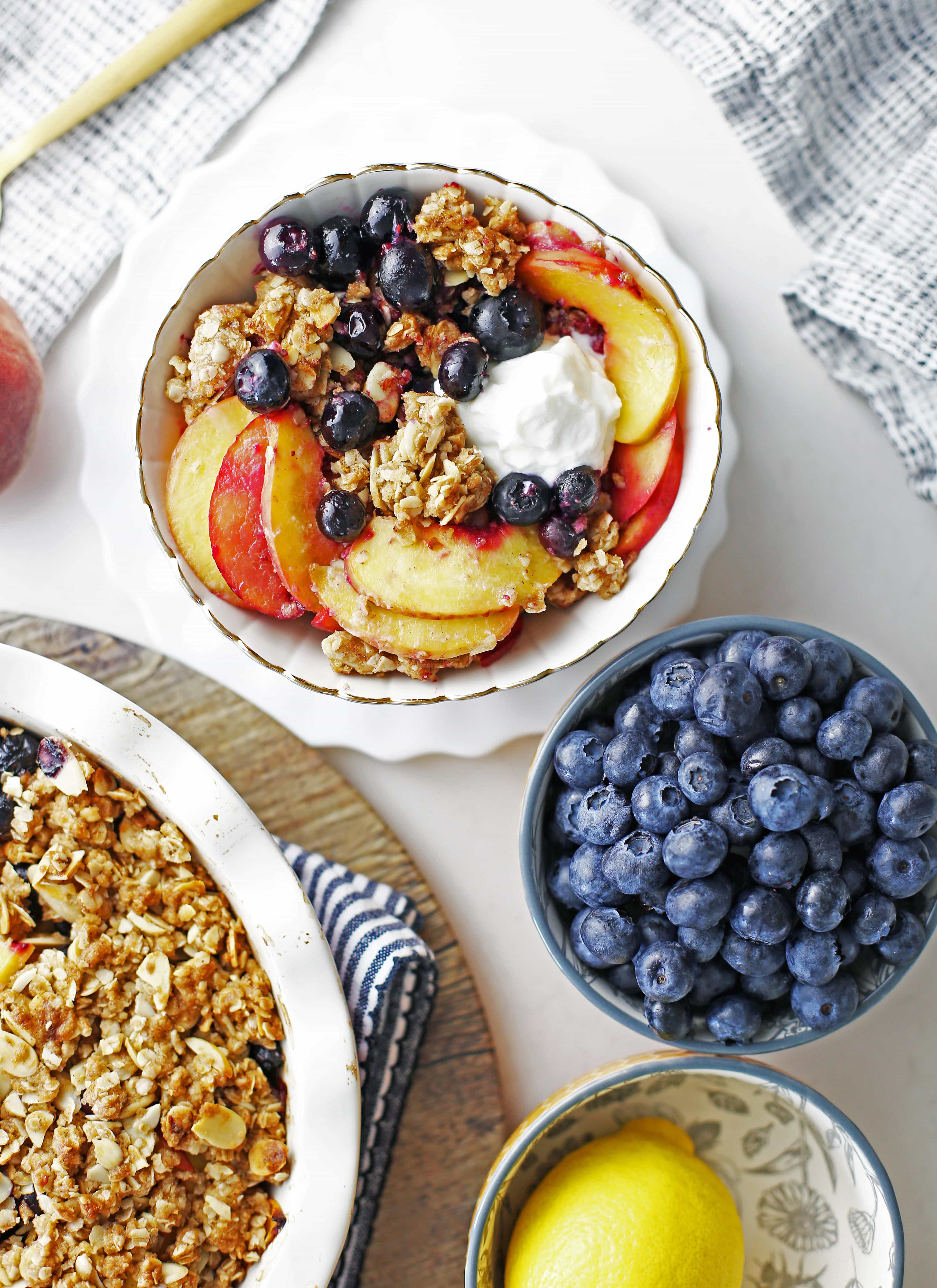 Overhead view of a pie dish and small bowl containing blueberry peach crisp with another bowl holding fresh blueberries.