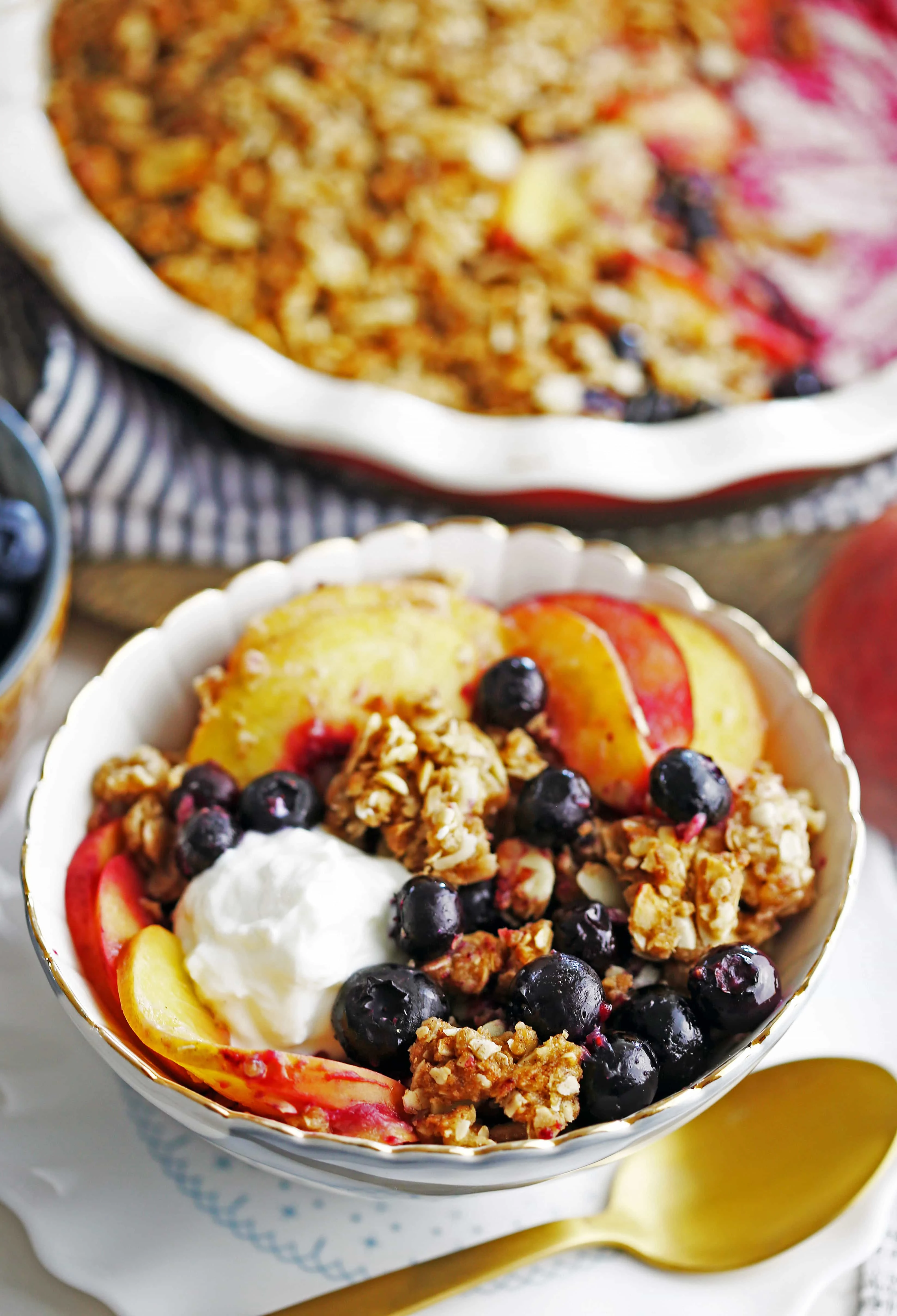 A closeup of a blue and white bowl containing blueberry peach crisp with a dollop of whipped cream.