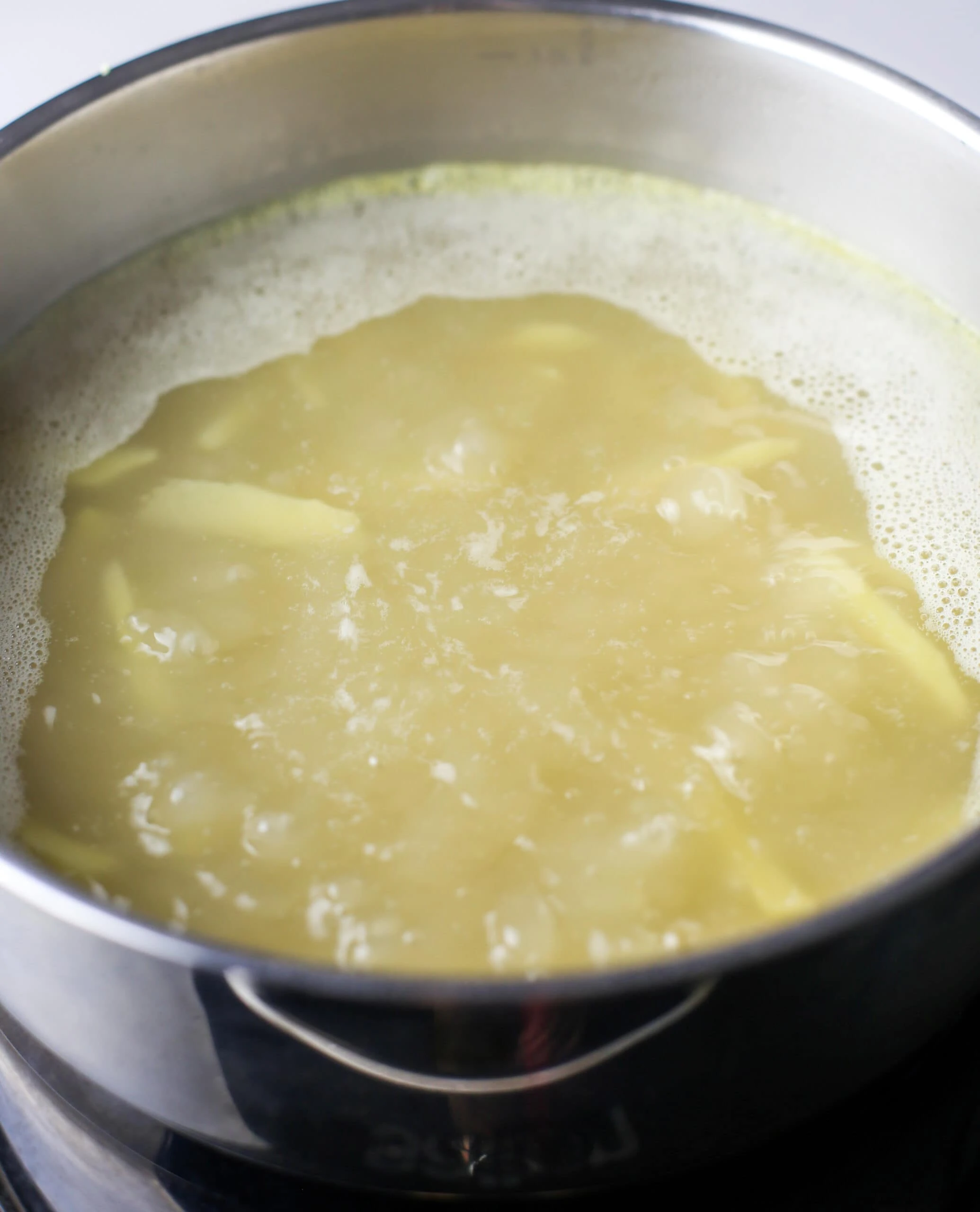 Boiling chicken broth and ginger slices in a large stainless steel pot.