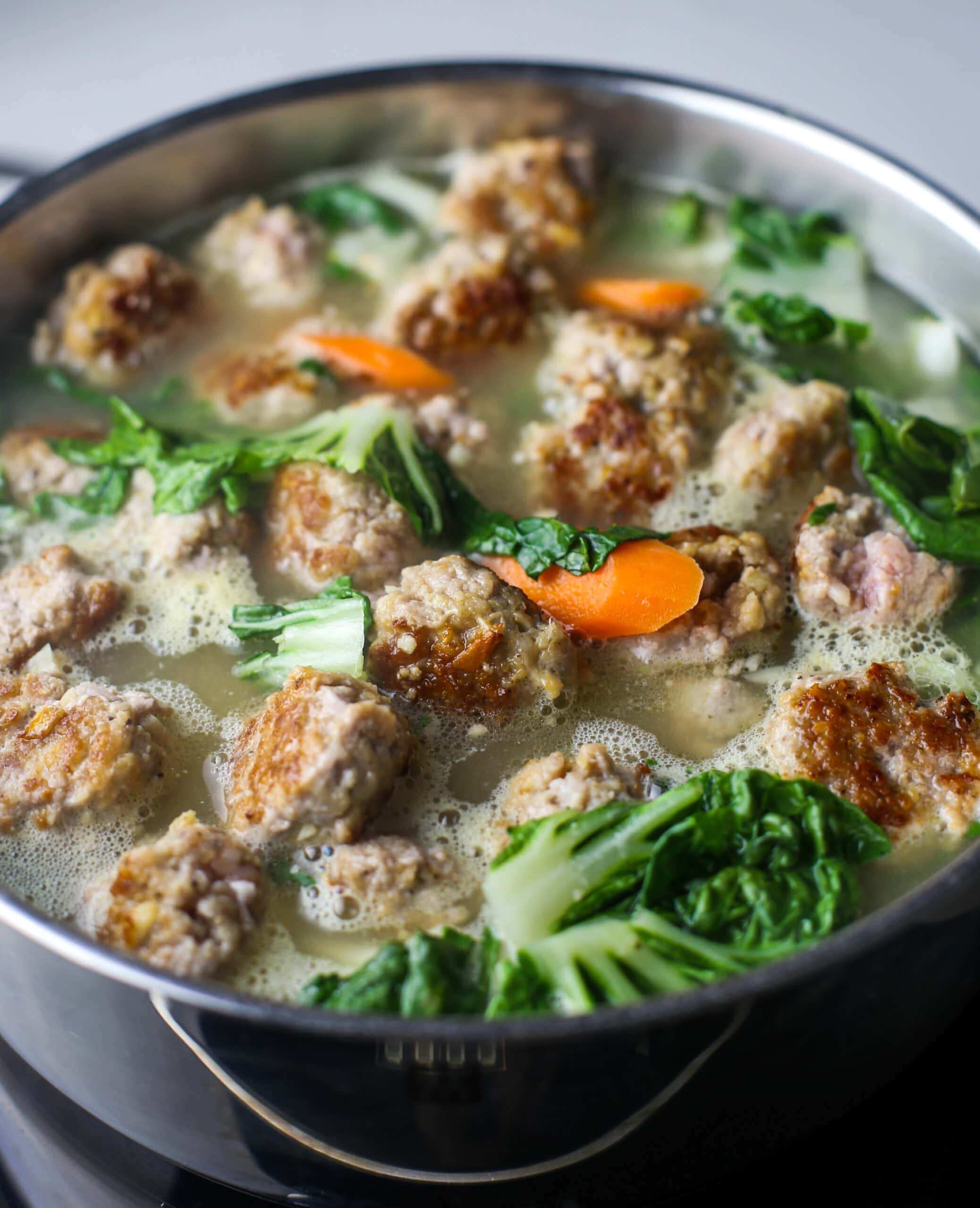 Ginger pork meatball soup with bok choy and carrots in a large stainless steel pot.