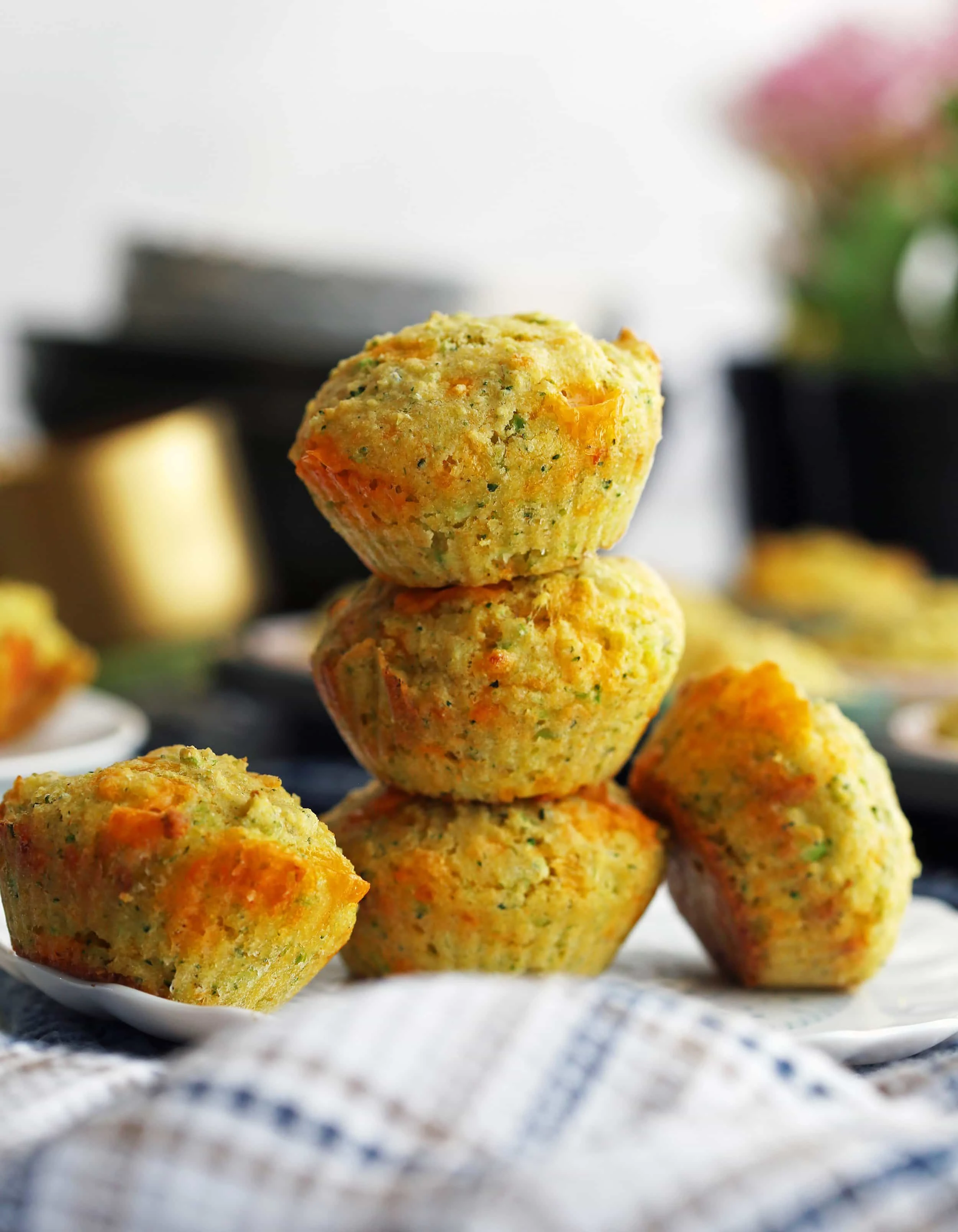 A side view of three Broccoli Cheddar Cornbread Muffins stacked on top one another with two more muffins on the side.