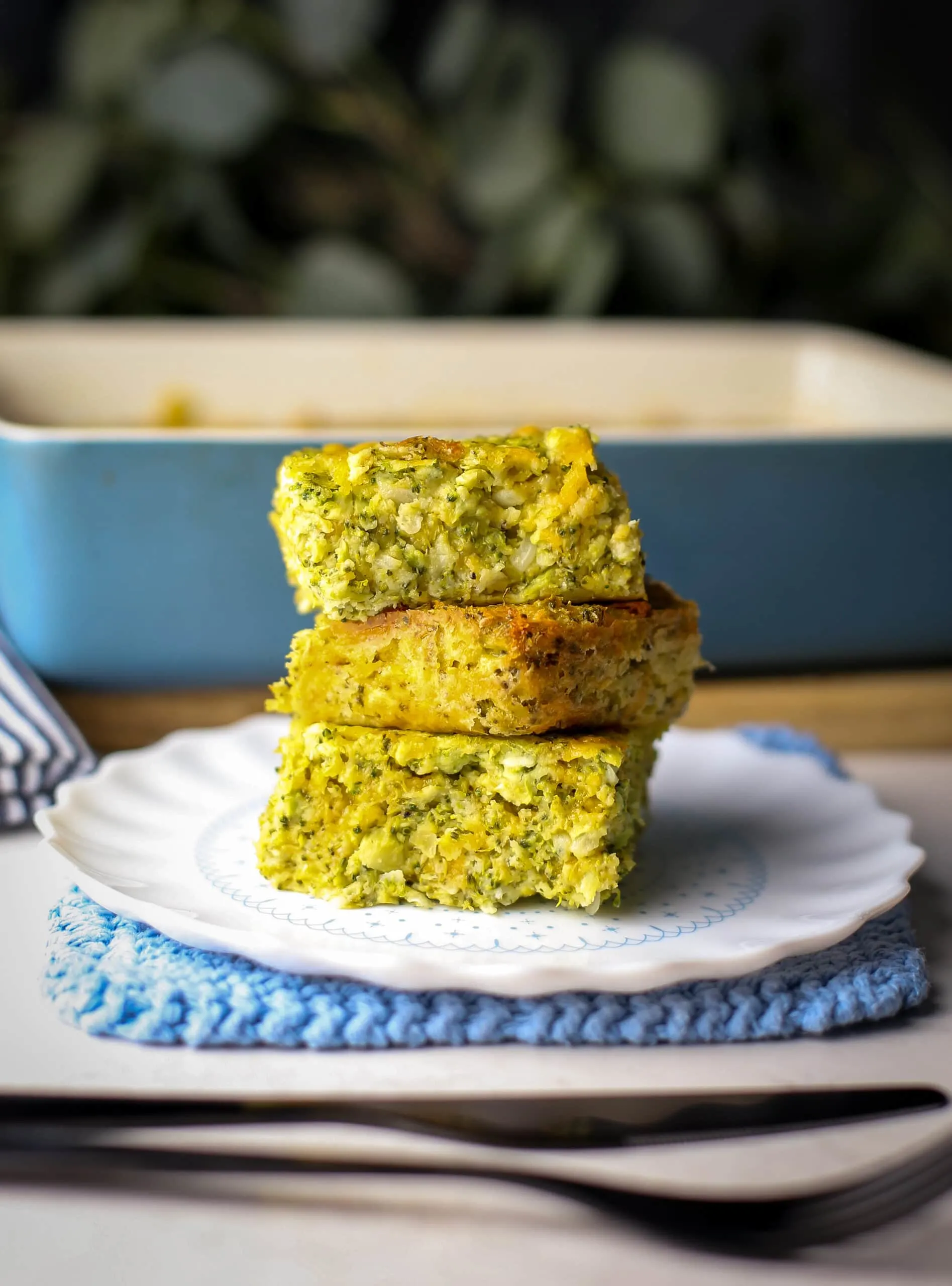 Three pieces of broccoli cheddar squares stacked on a white plate.