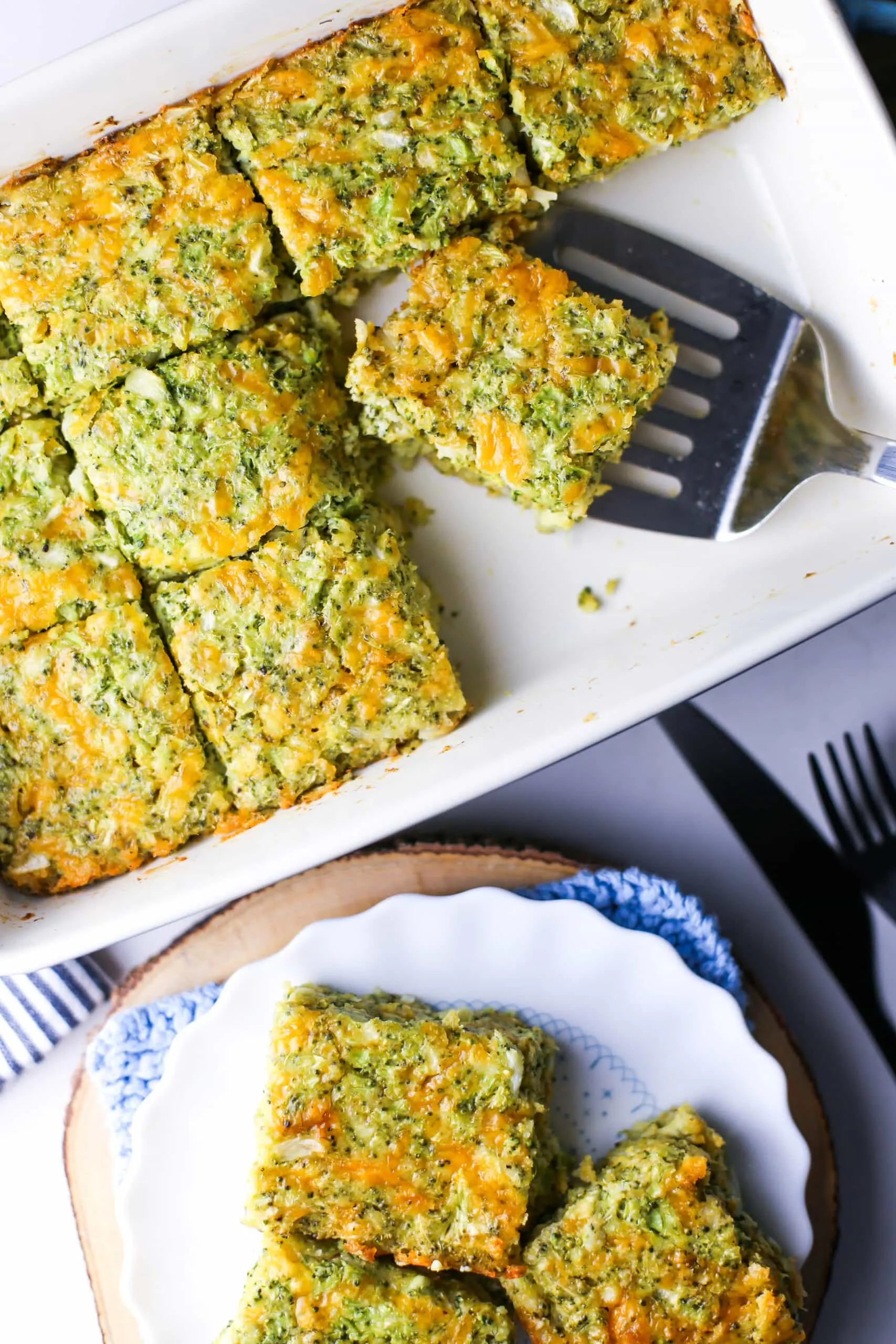 Overhead view of broccoli cheddar squares on a rectangular baking dish and white plate.