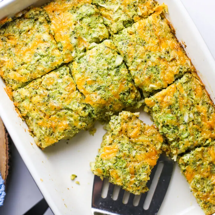 Overhead view of broccoli cheddar squares on a rectangular baking dish with a metal spatula.