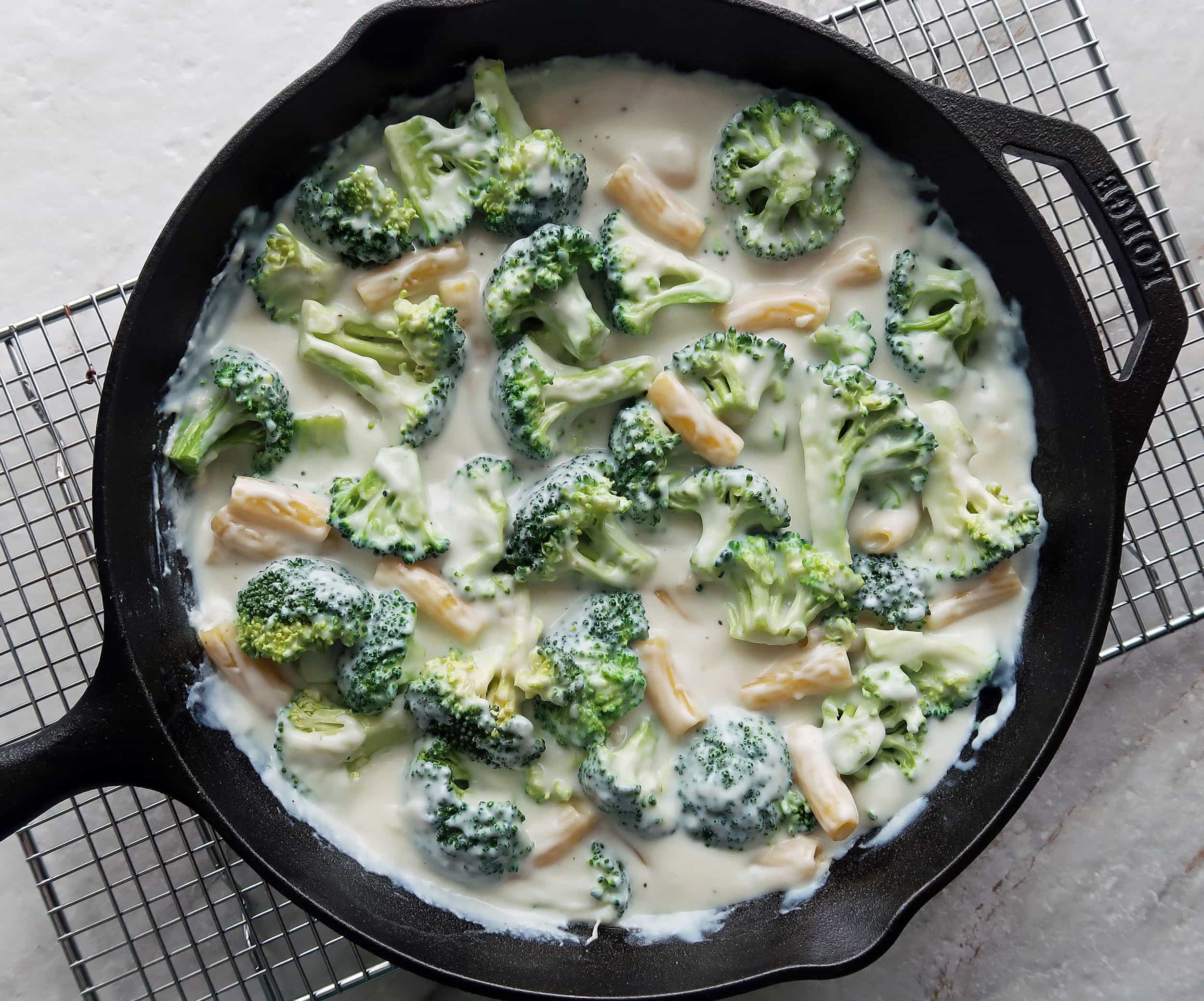 Broccoli, pasta, and milk in a skillet.
