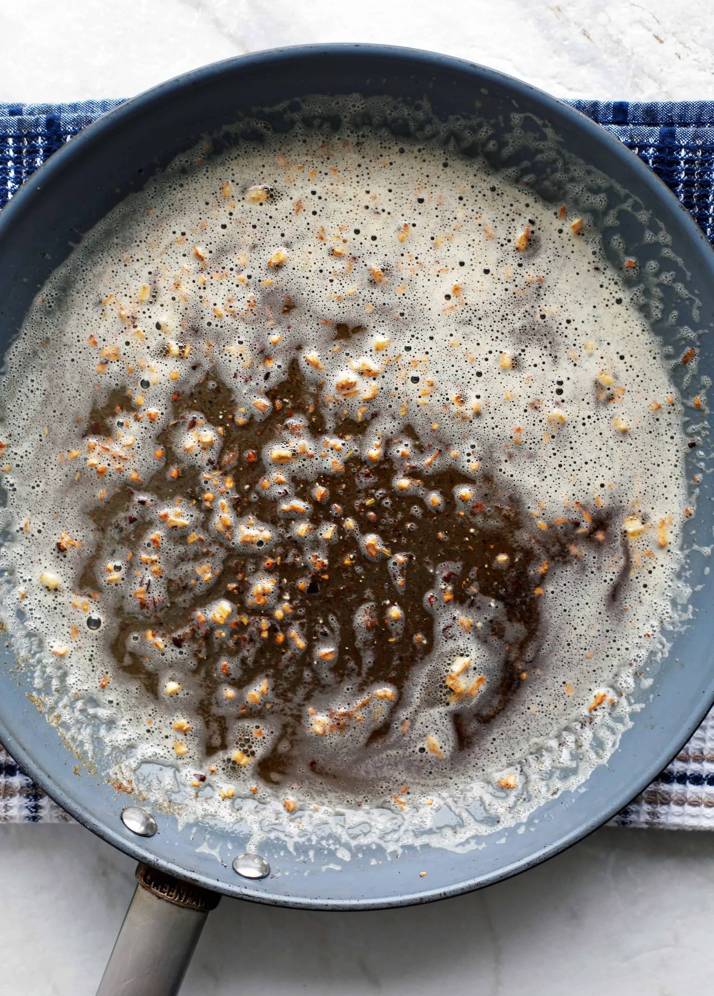 Brown butter with toasted minced garlic and spices in a large light blue skillet.