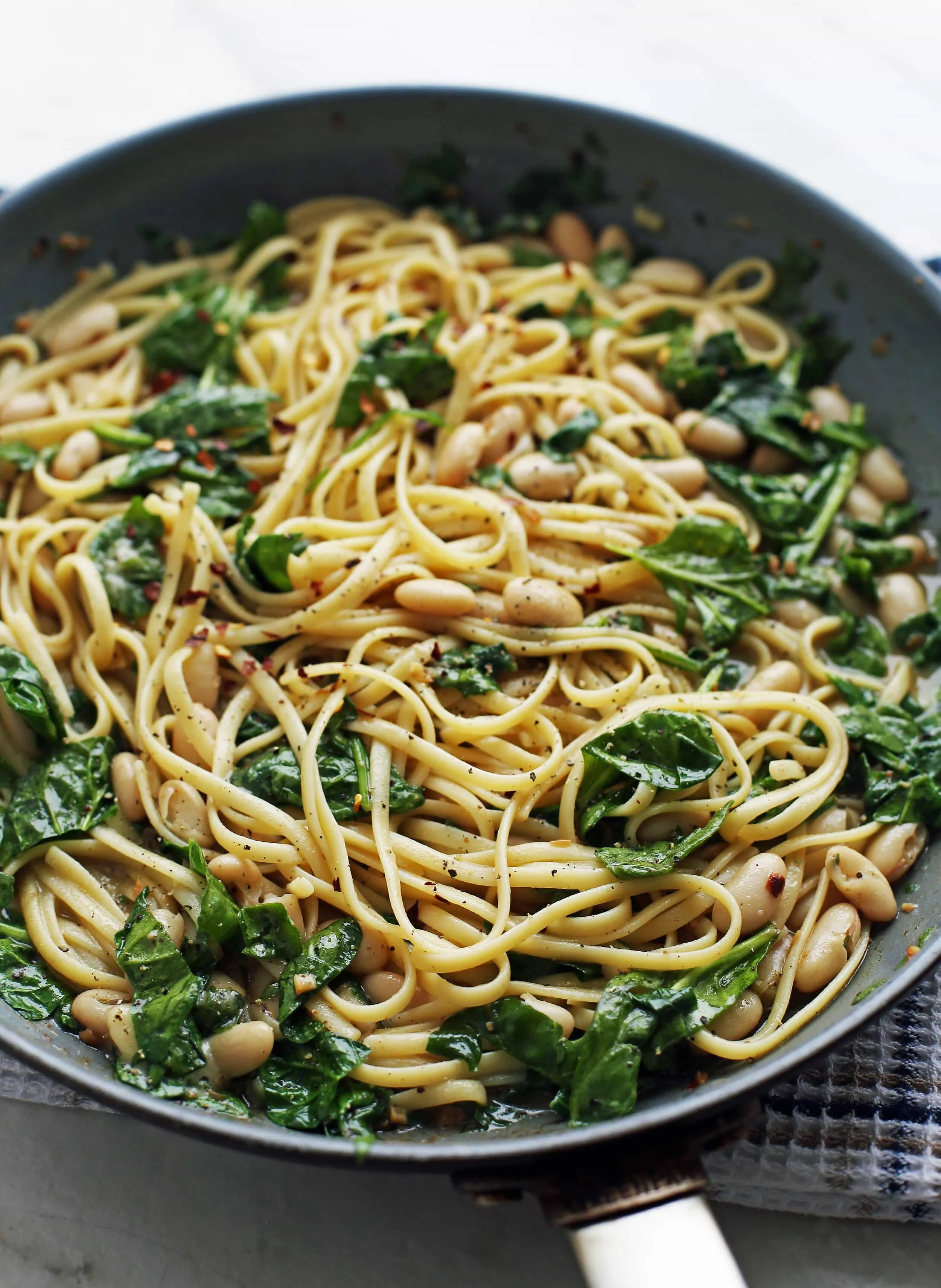 Tossed brown butter linguine pasta with spinach and white beans in a large skillet.