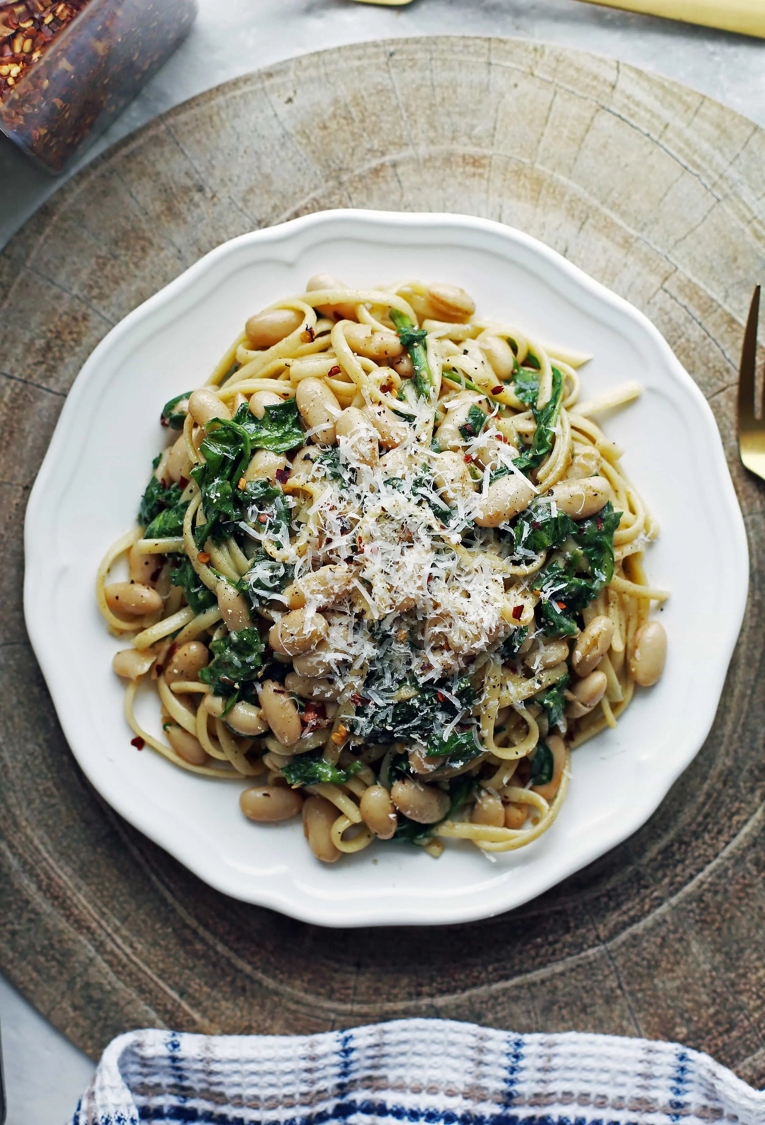 Overhead view of Brown Butter Linguine with White Beans and Spinach topped with parmesan cheese on a white plate.