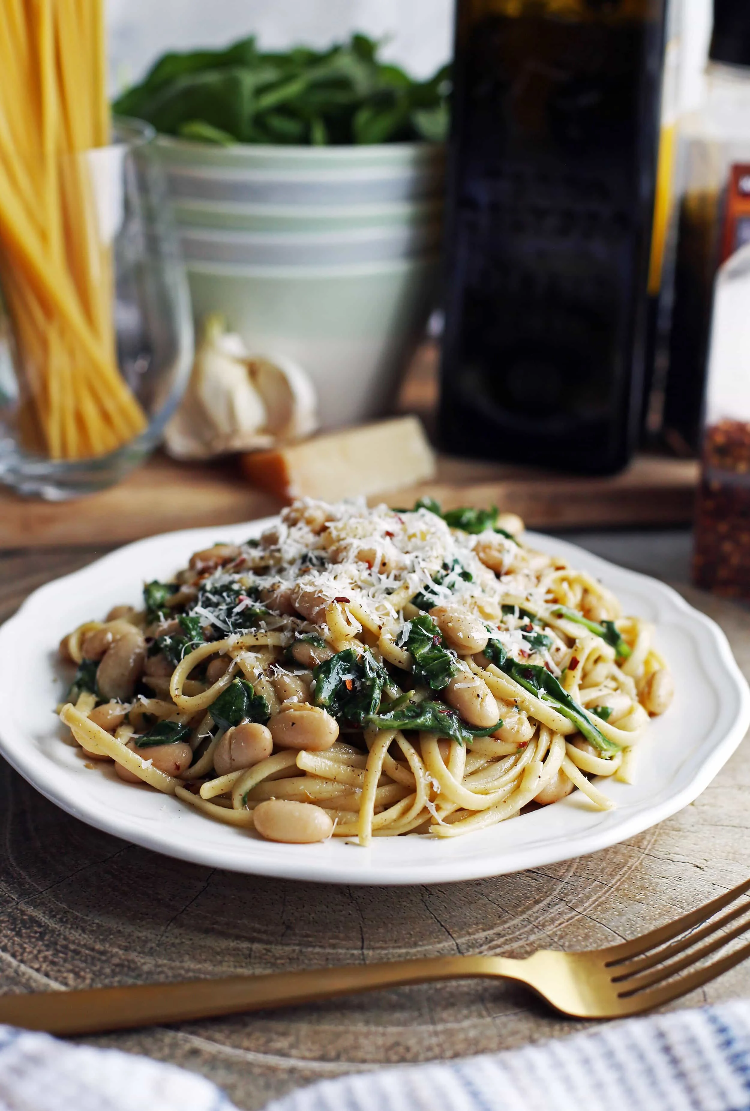 A white plate full of Brown Butter Linguine with White Beans and Spinach topped with parmesan cheese.