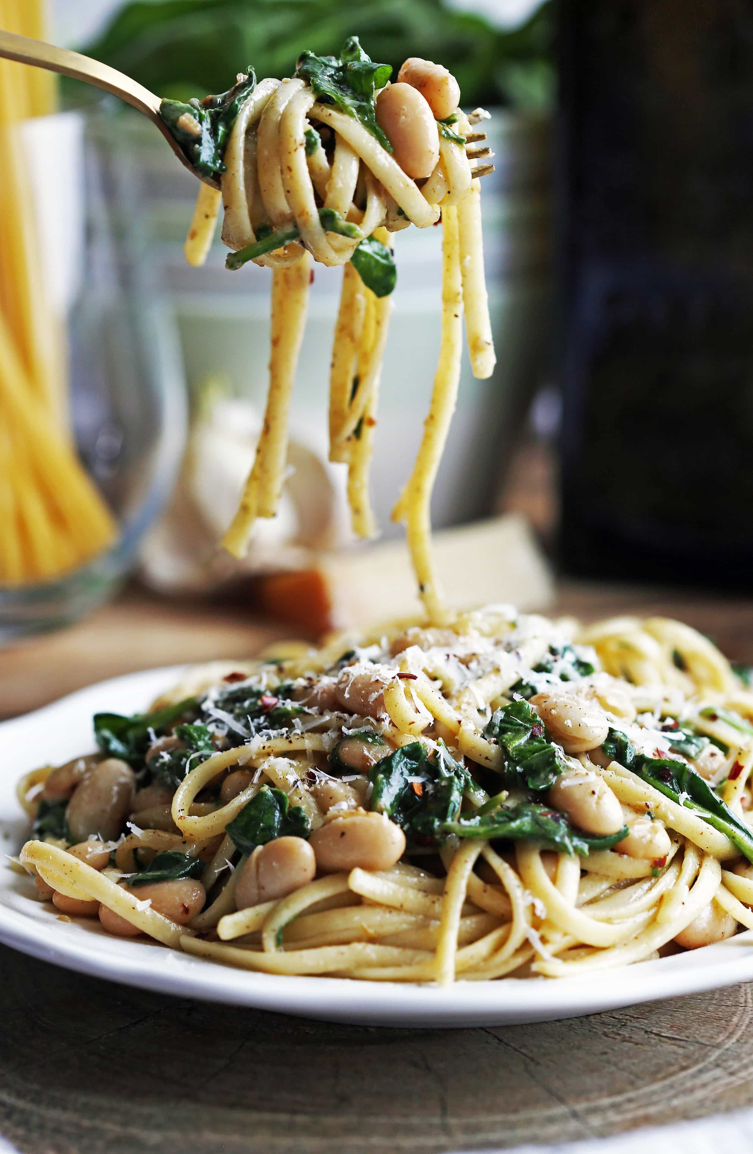 Brown Butter Linguine with White Beans and Spinach twirled on a gold fork with a plateful of the same pasta below.