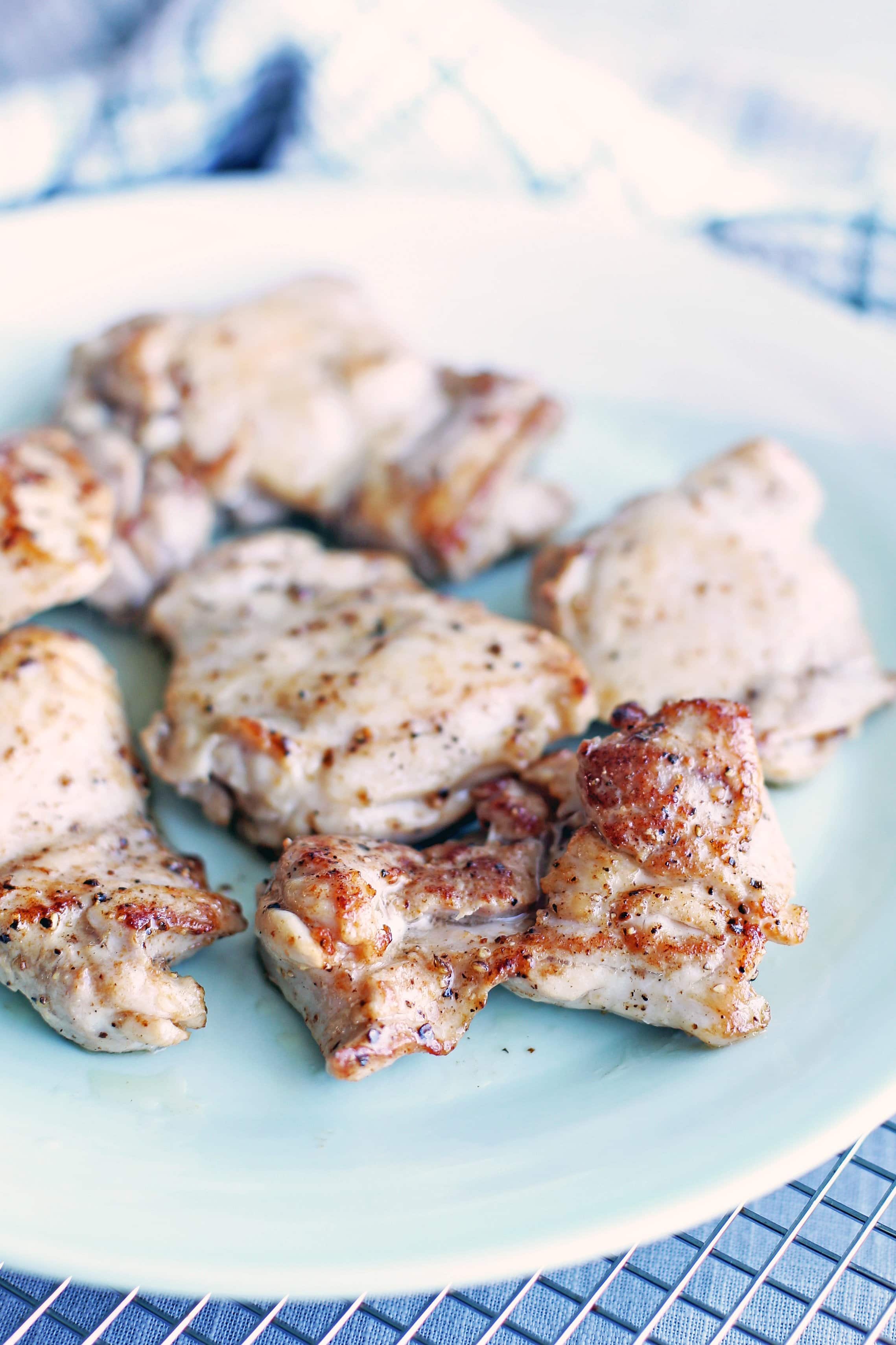 Six browned chicken thighs on a light green plate.