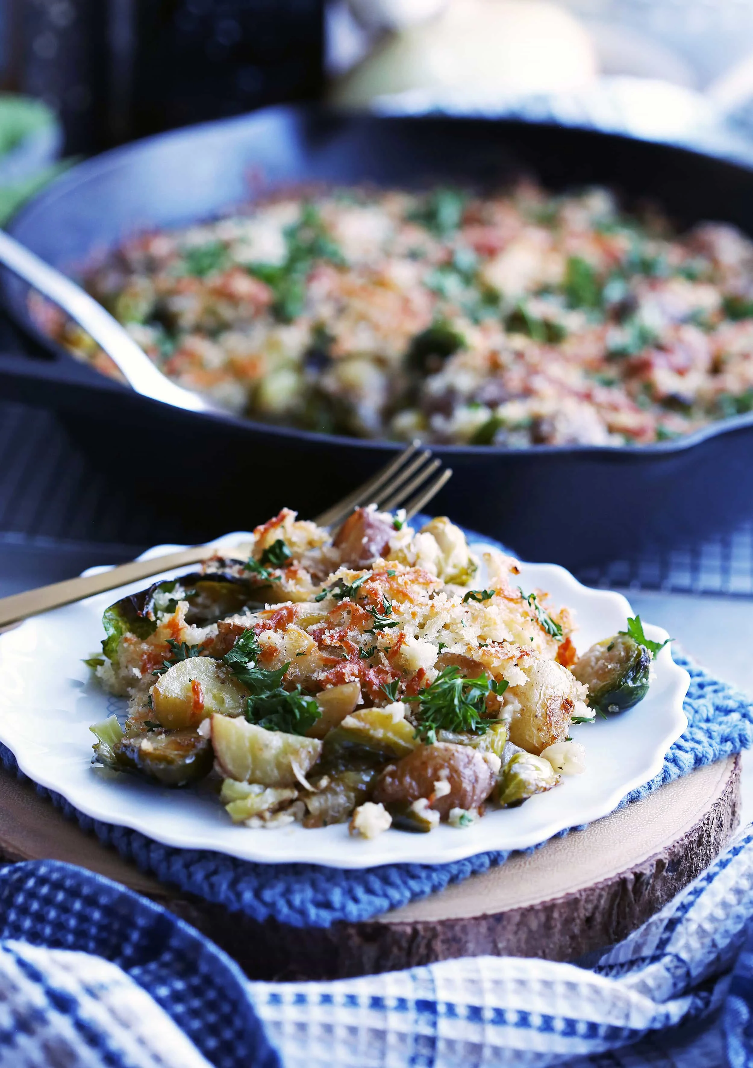 Brussels Sprouts and Potato Gratin on a white plate with a plate with more in a cast iron skillet behind the plate.