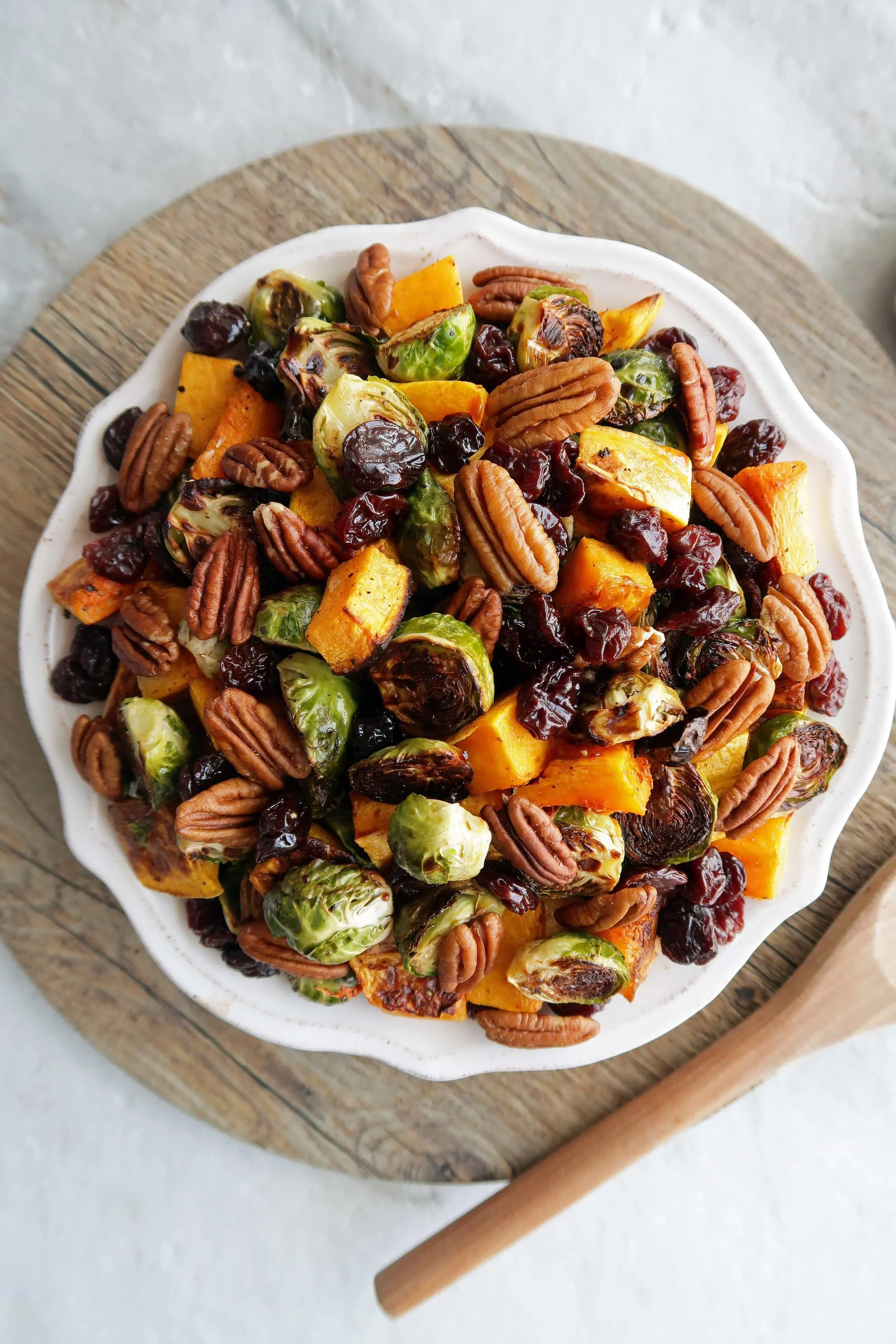Roasted butternut squash and Brussels sprouts with pecans and dried cherries on a white plate.