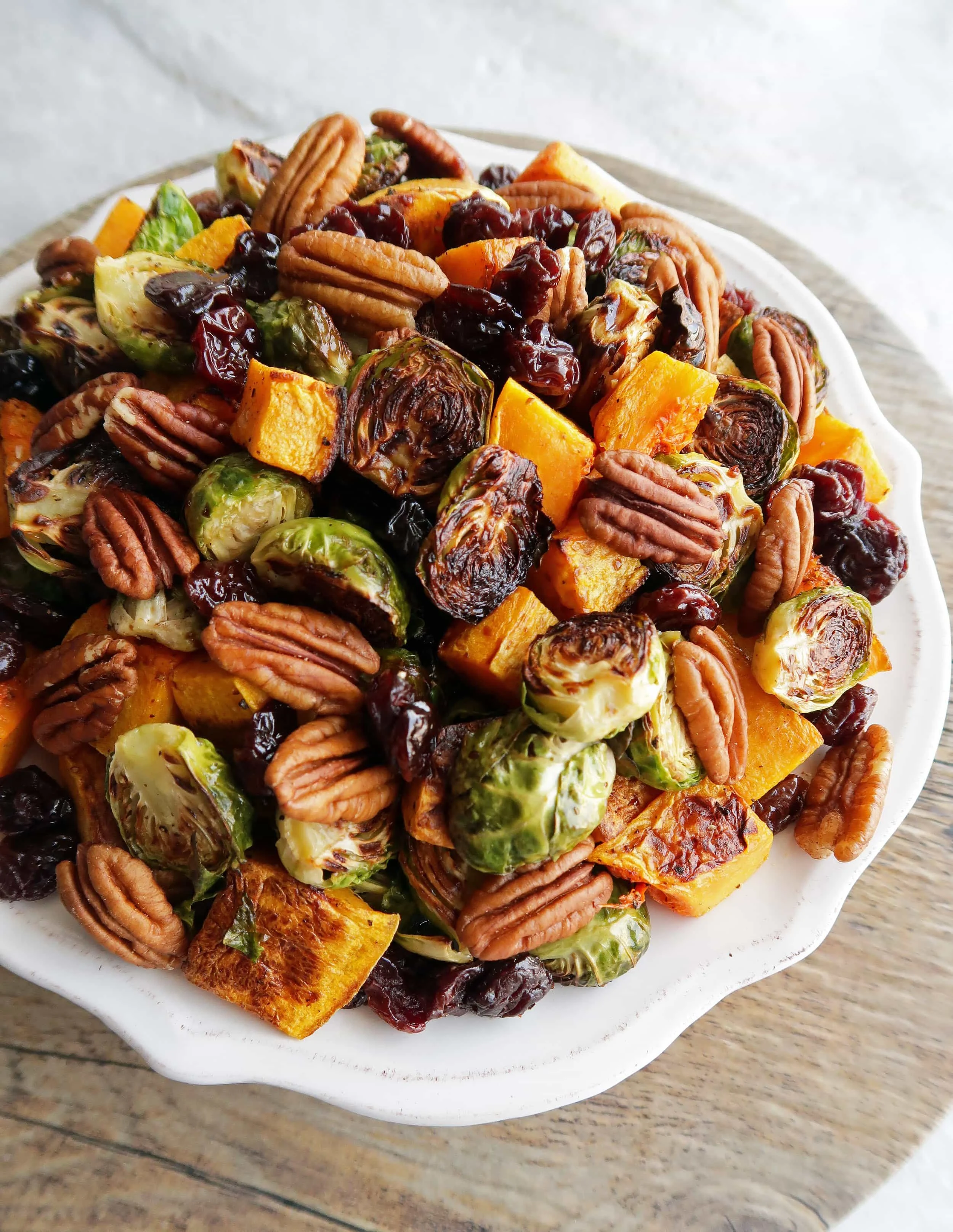 White plate of roasted butternut squash and Brussels sprouts with pecans and dried cherries.