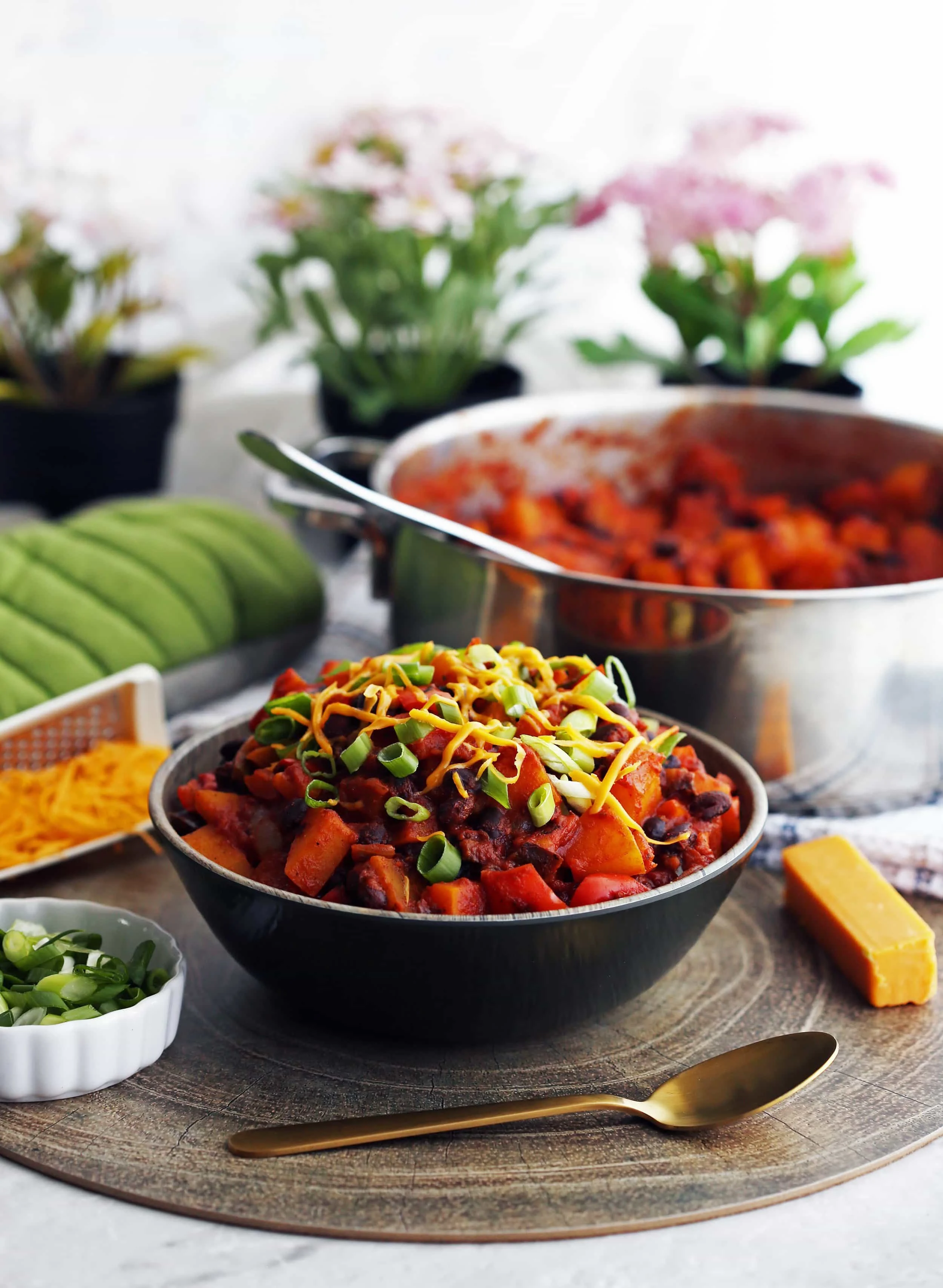 Roasted Butternut Squash and Black Bean Chili topped with green onions and shredded cheese in a wooden bowl.