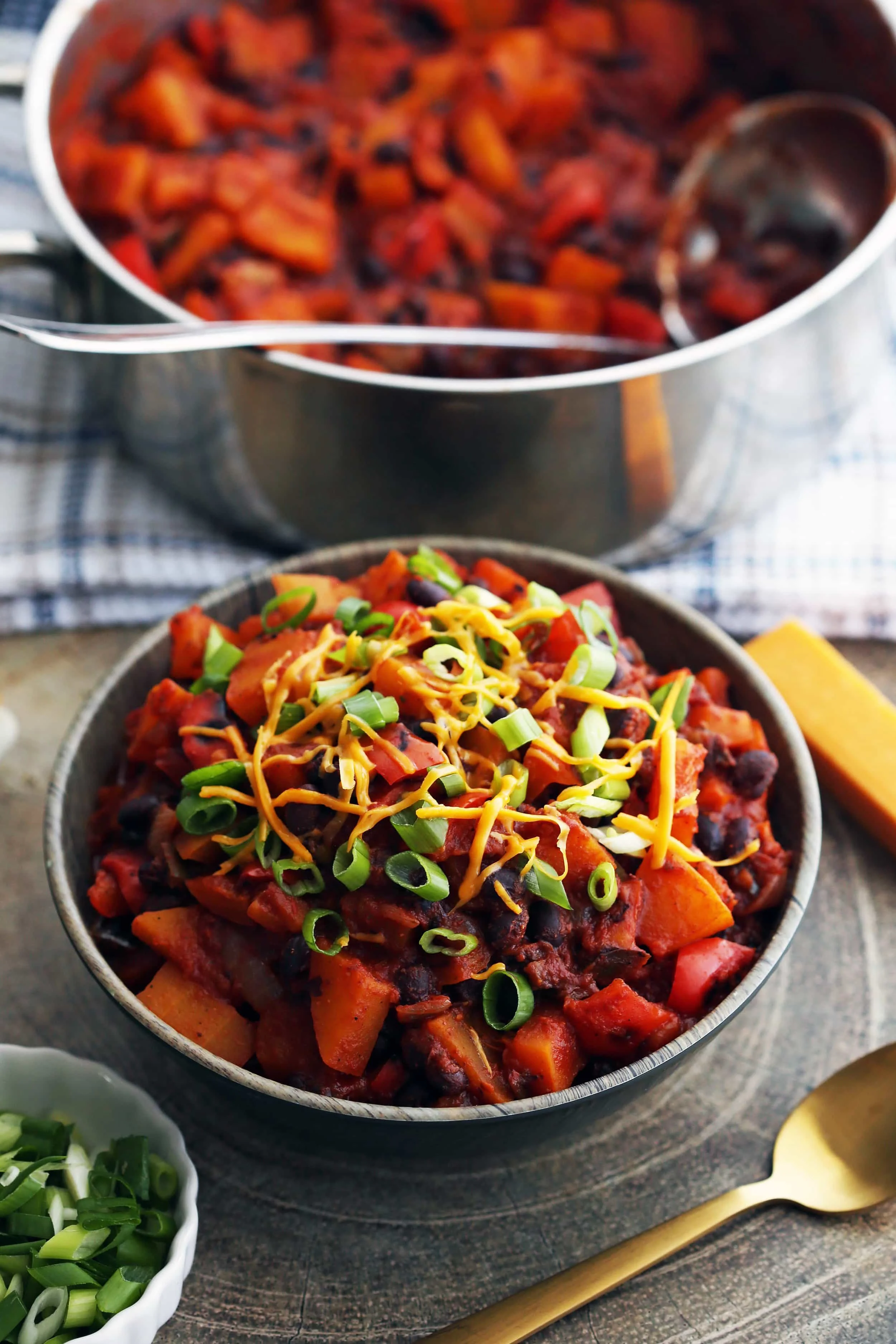 A bowl of Roasted Butternut Squash and Black Bean Chili with green onions and shredded cheese on top.