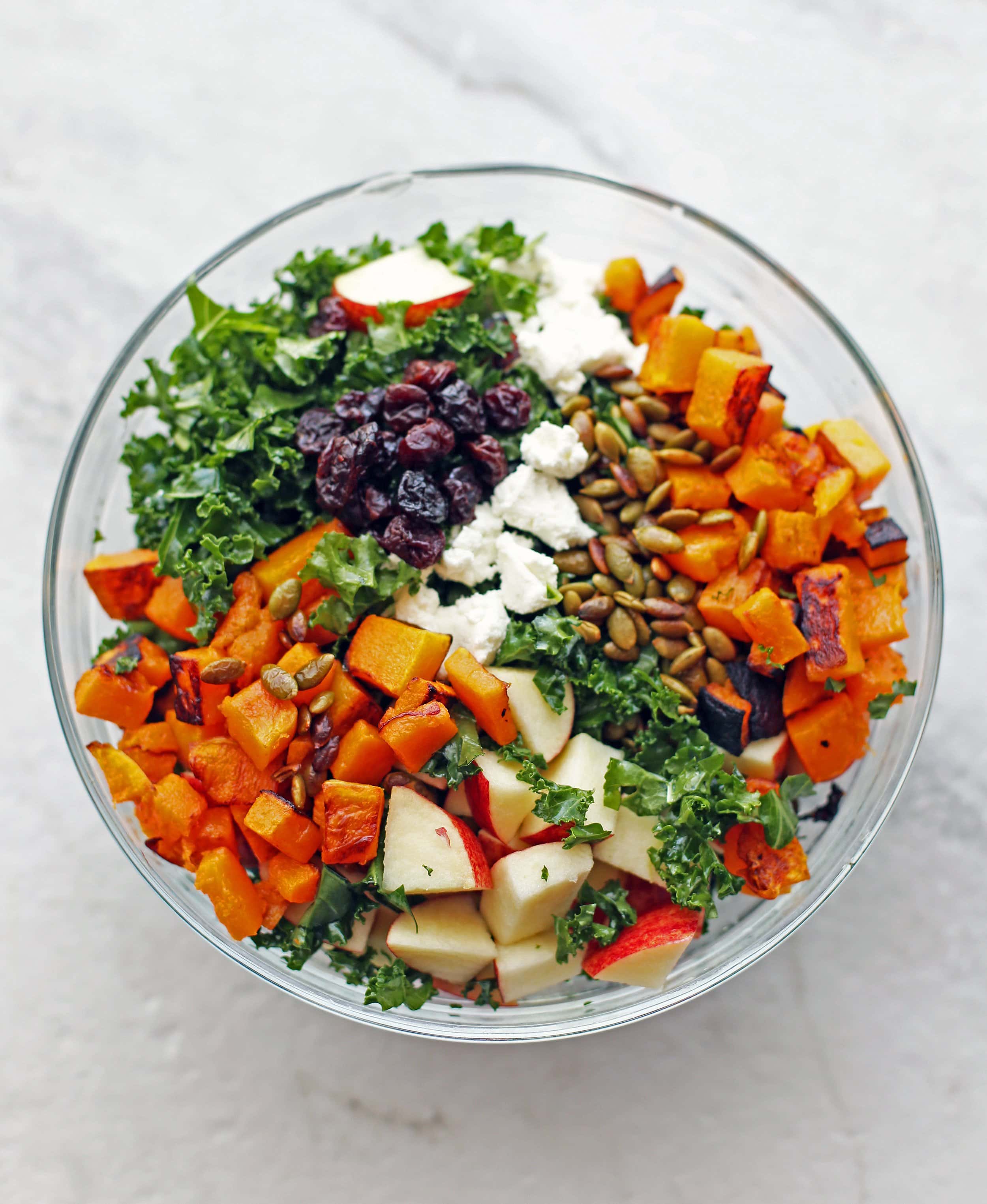A bowl filled with kale, apples, roasted butternut squash, goat cheese, dried cherries, and pumpkin seeds.