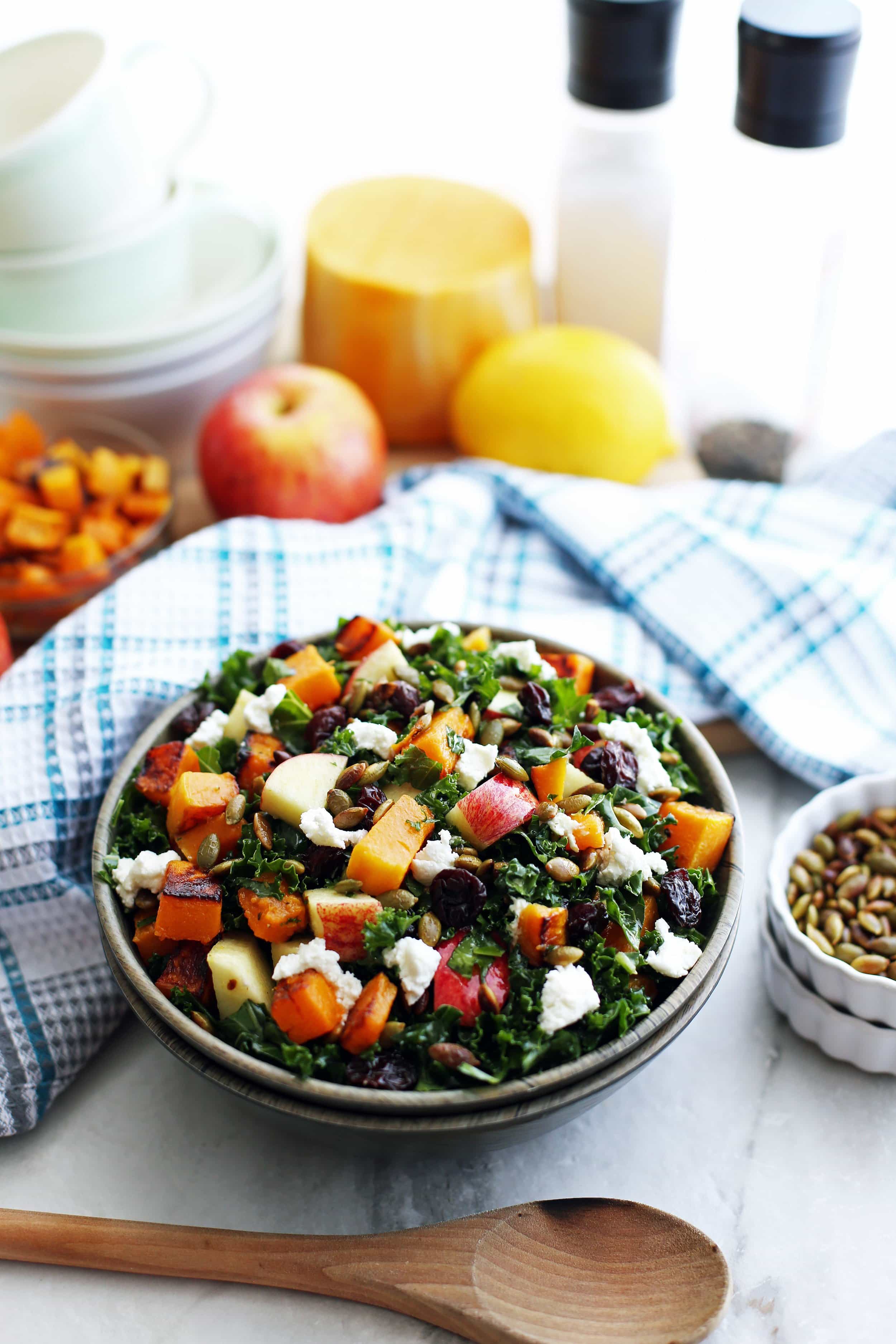 Bowl of kale salad with roasted butternut squash, apple, goat cheese, pumpkin seeds, and dried cherries.
