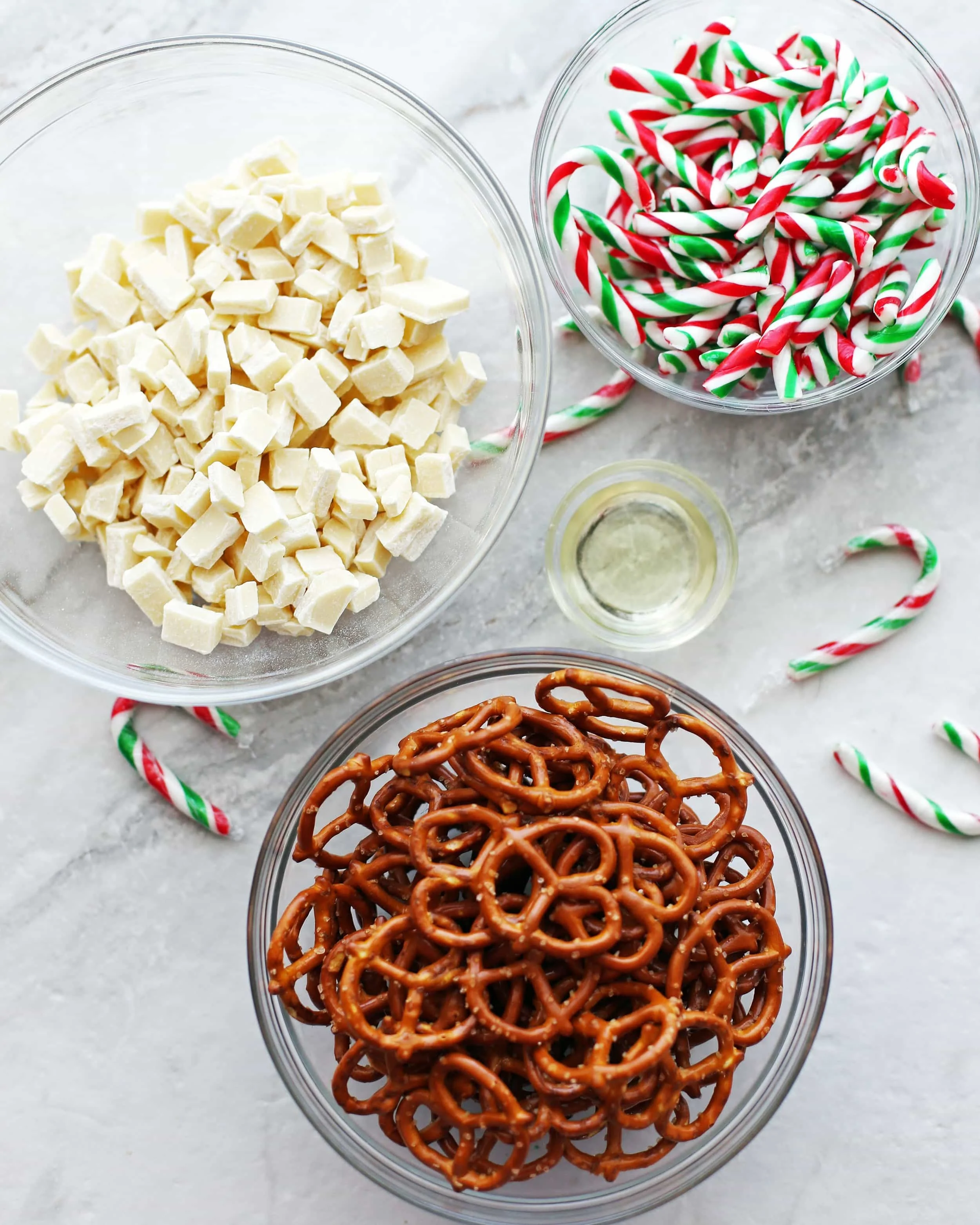 Four glass bowls with mini pretzels, mini peppermint candy canes, white chocolate, and vegetable oil.