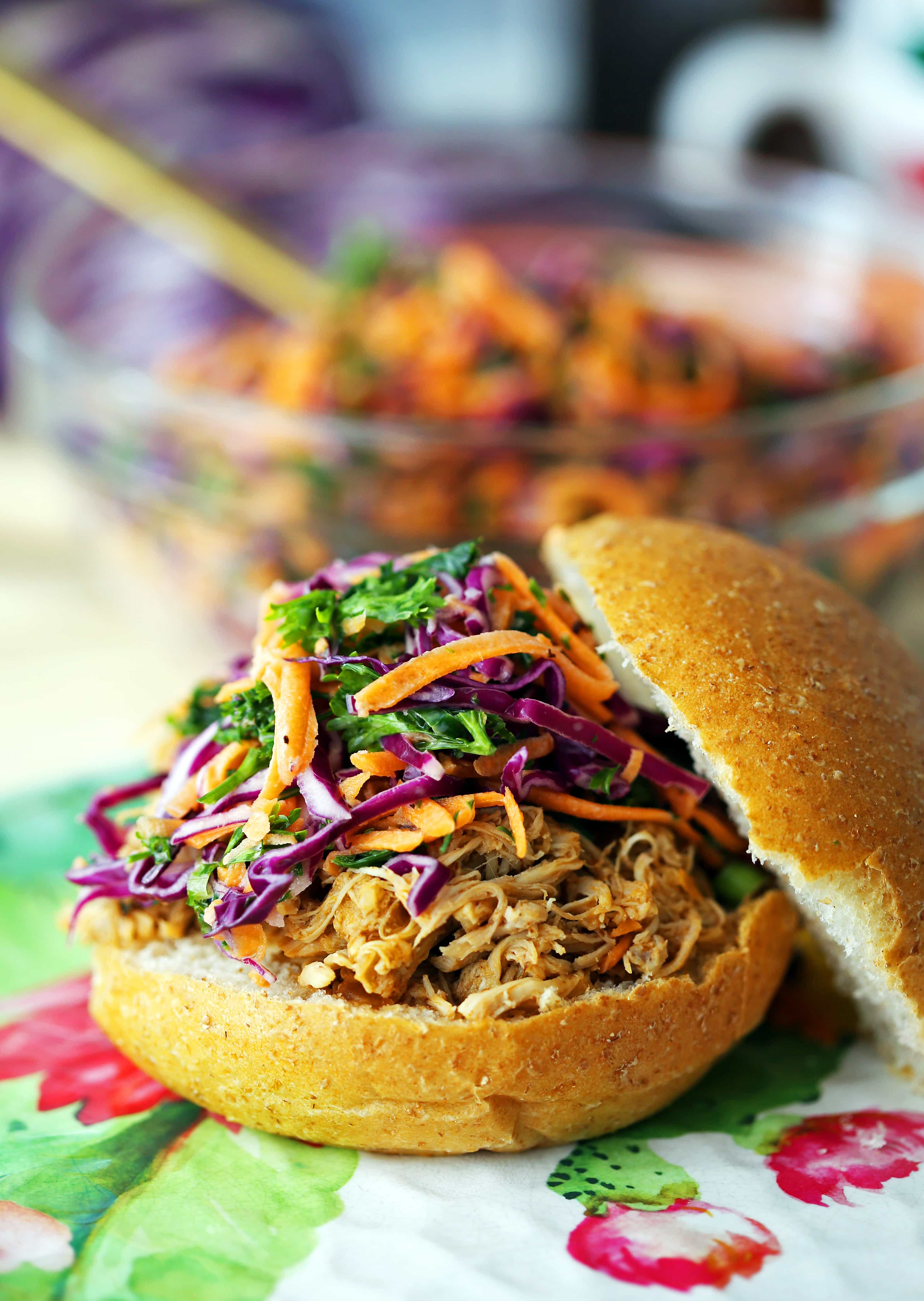 A bun with shredded barbecue chicken and carrot cabbage coleslaw on top.