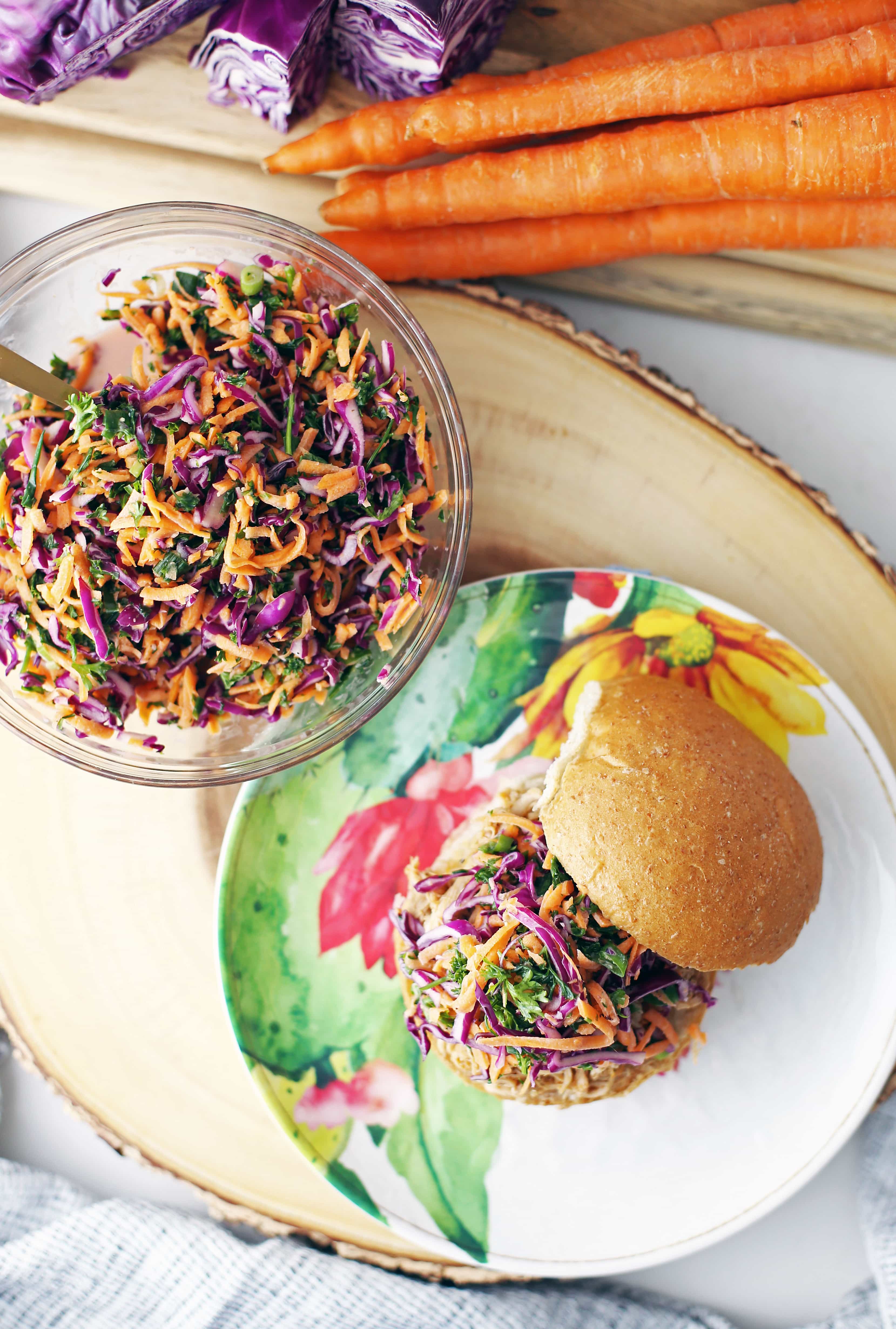 Overhead view of a glass bowl containing carrot cabbage coleslaw and a shredded chicken burger with coleslaw on top on a plate.