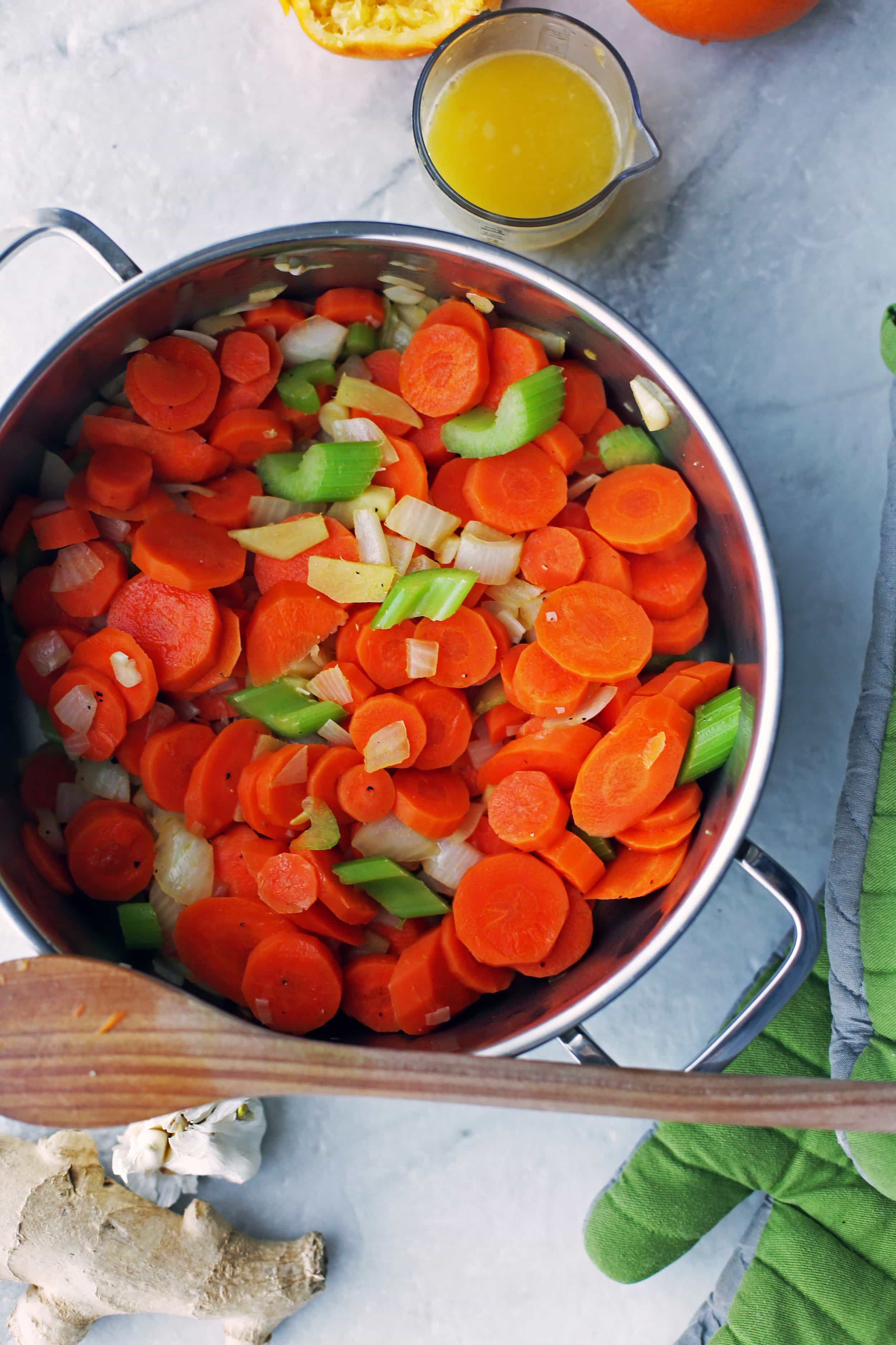 Ingredients for carrot orange ginger soup in a large pot with wooden spoon to the side.