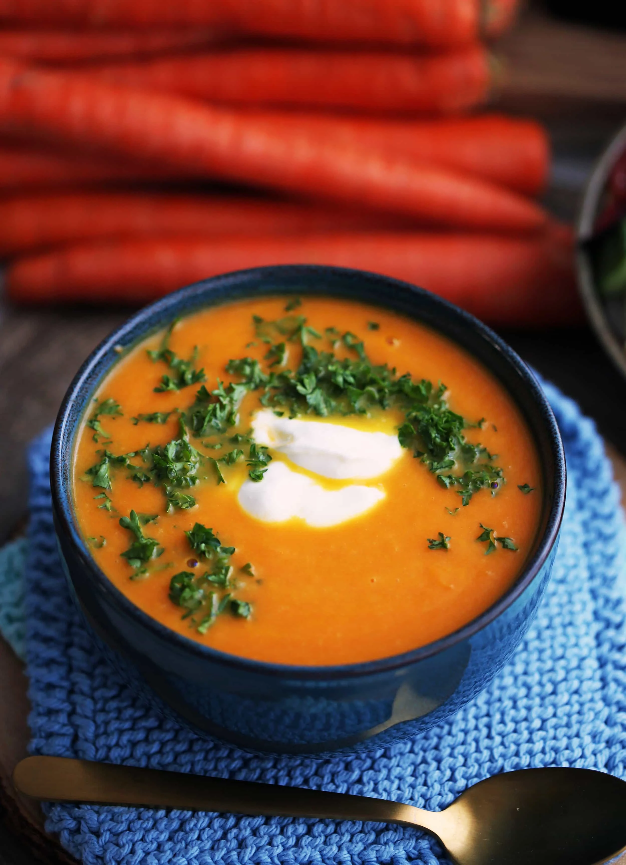 A full bowl of vegan and gluten-free Carrot Orange Ginger Soup in a blue bowl with a gold spoon beside it.