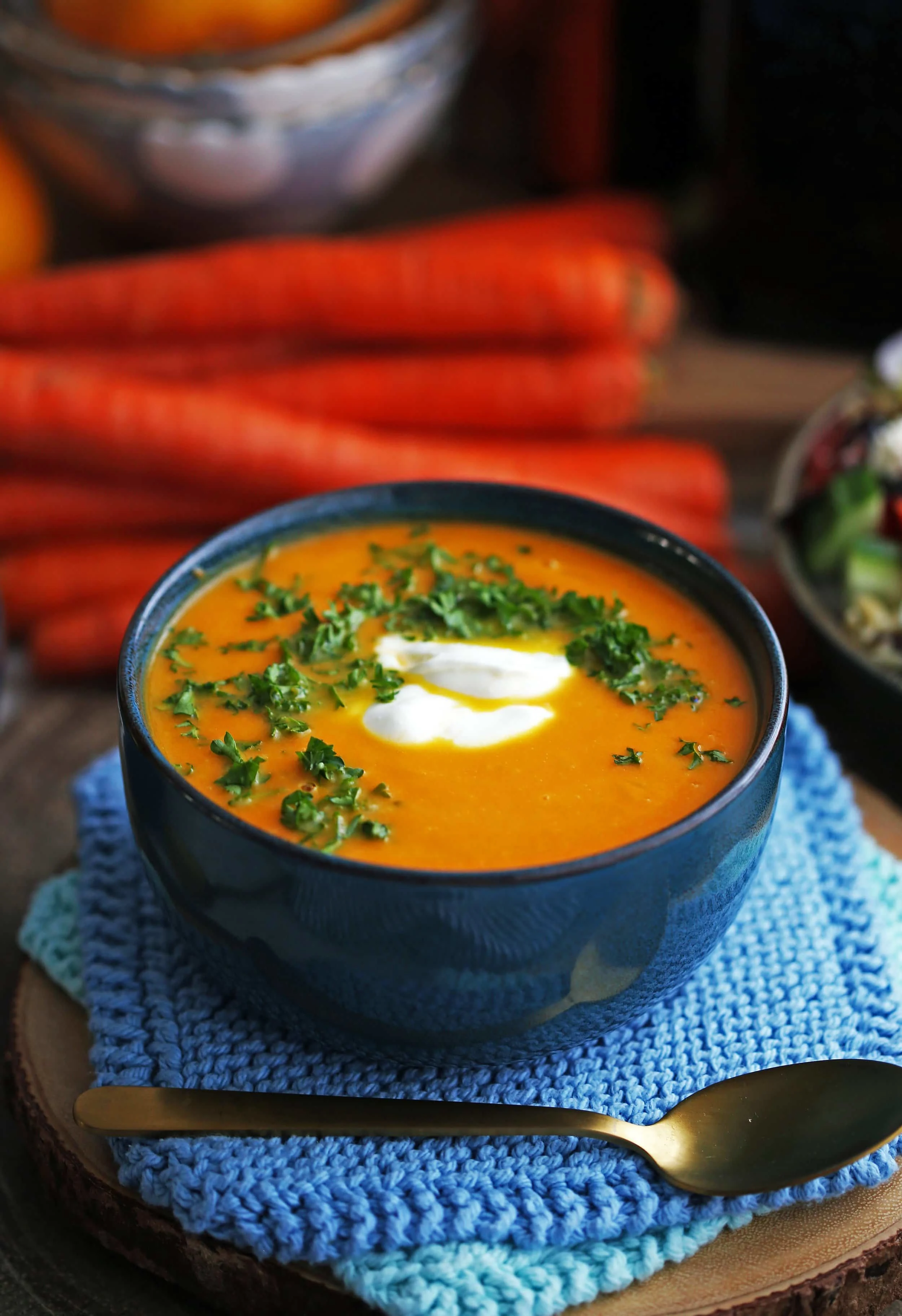 Healthy Carrot Orange Ginger Soup garnished with whipped coconut cream and chopped parsley in a blue bowl.