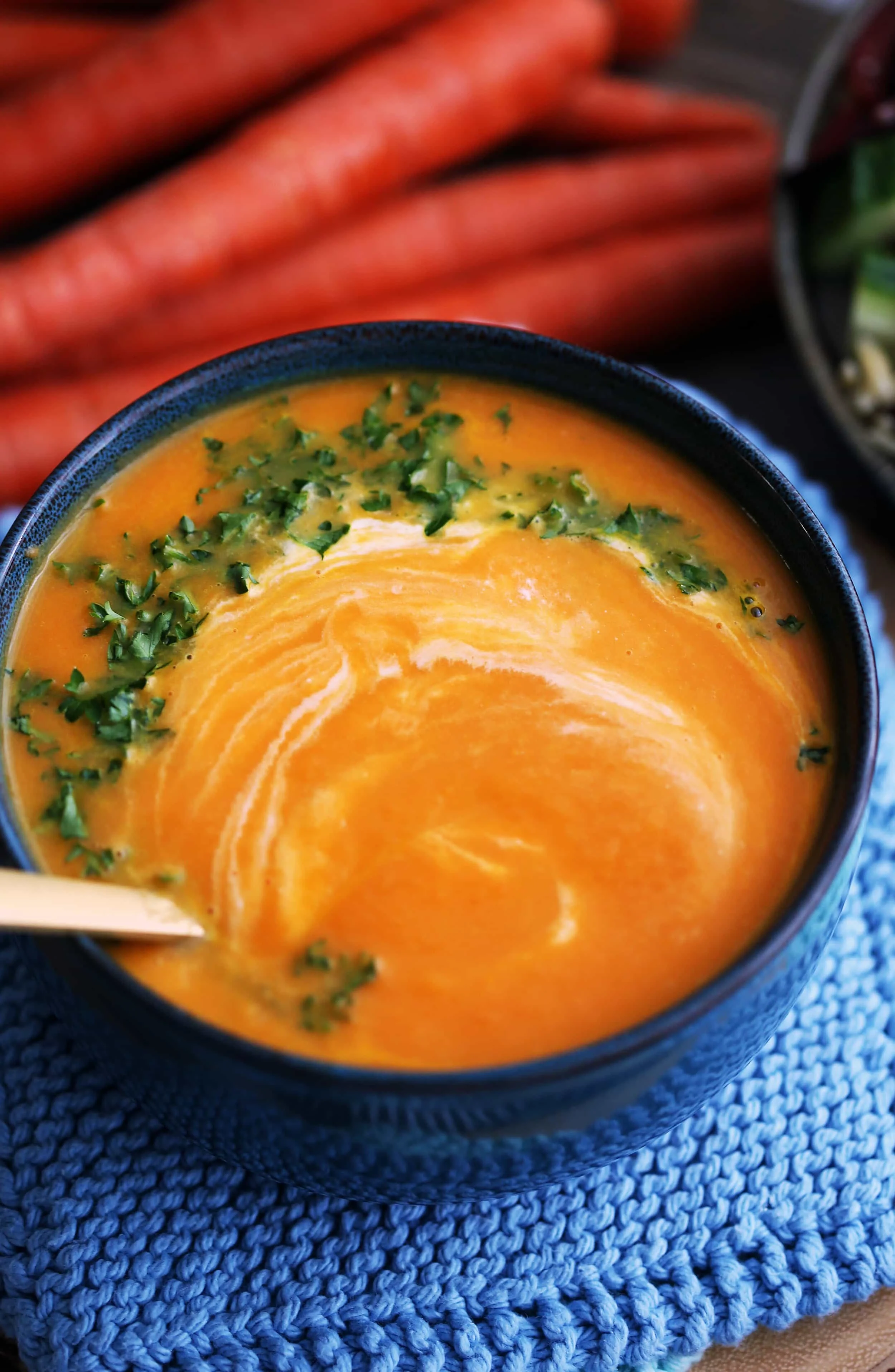 A full bowl of vegan Carrot Orange Ginger Soup with whipped coconut cream and chopped parsley stirred into it using a gold spoon.