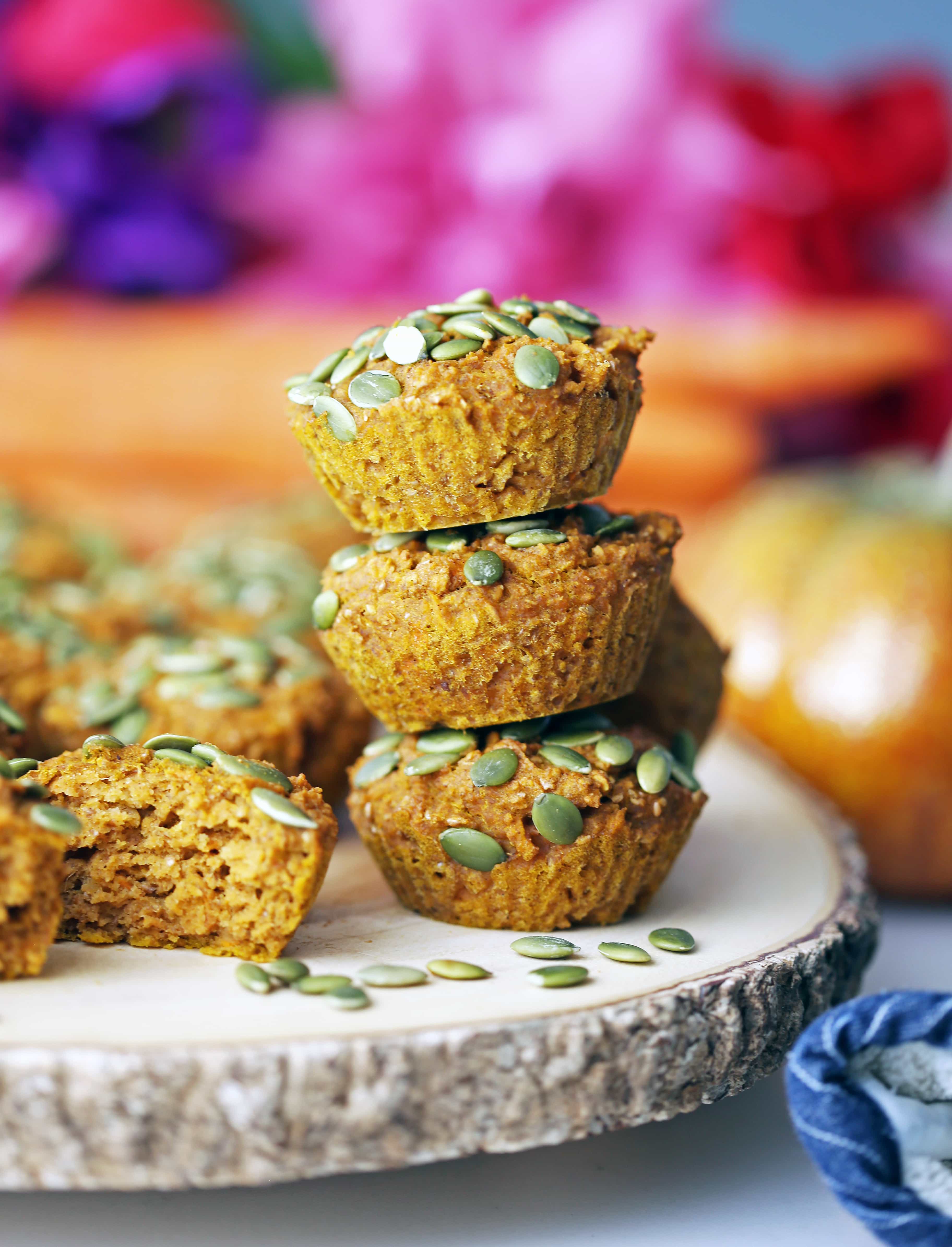 Three carrot pumpkin muffins stacked on top one another on a wooden board.