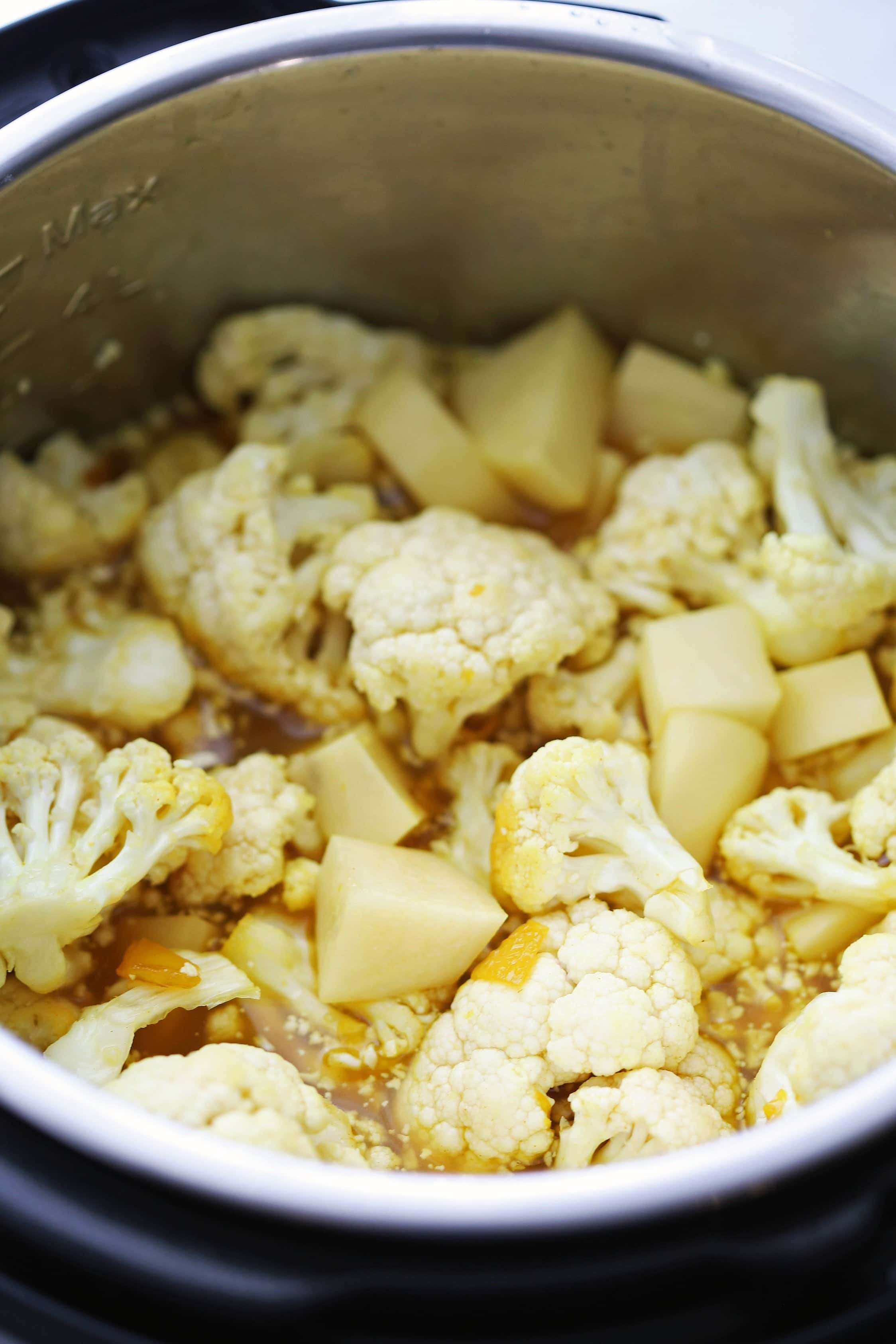 Sautéed spiced onions, garlic, and ginger topped with vegetable broth. cauliflower florets, and chopped potatoes in the Instant Pot.